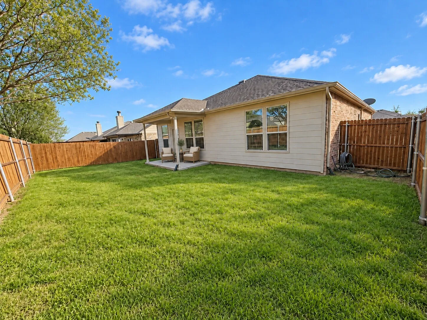 Expansive fenced yard featuring a covered patio, brick and siding exterior, and mature tree