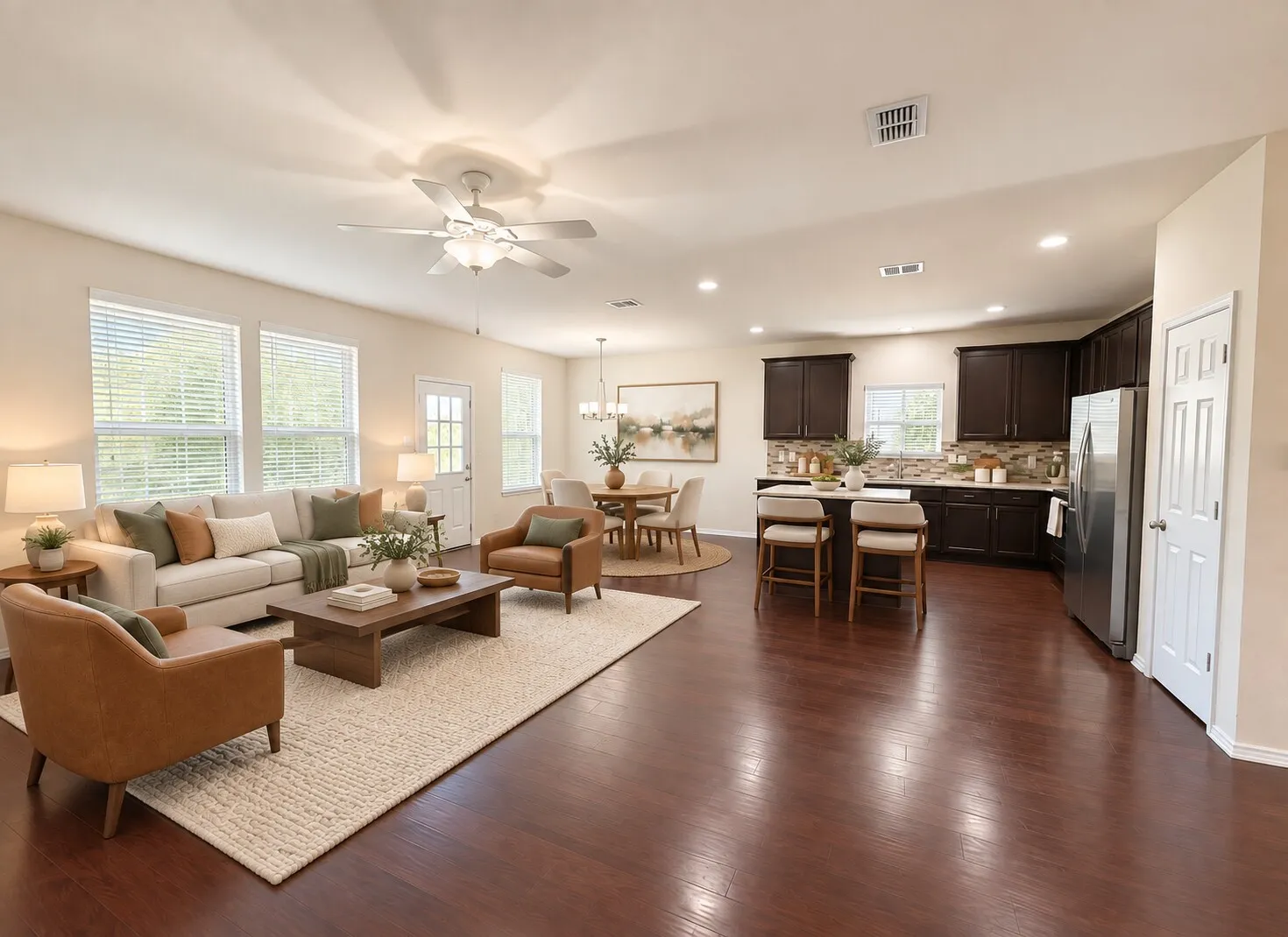 Expansive living area with wood-finish flooring, ample natural light from multiple windows, and a ceiling fan