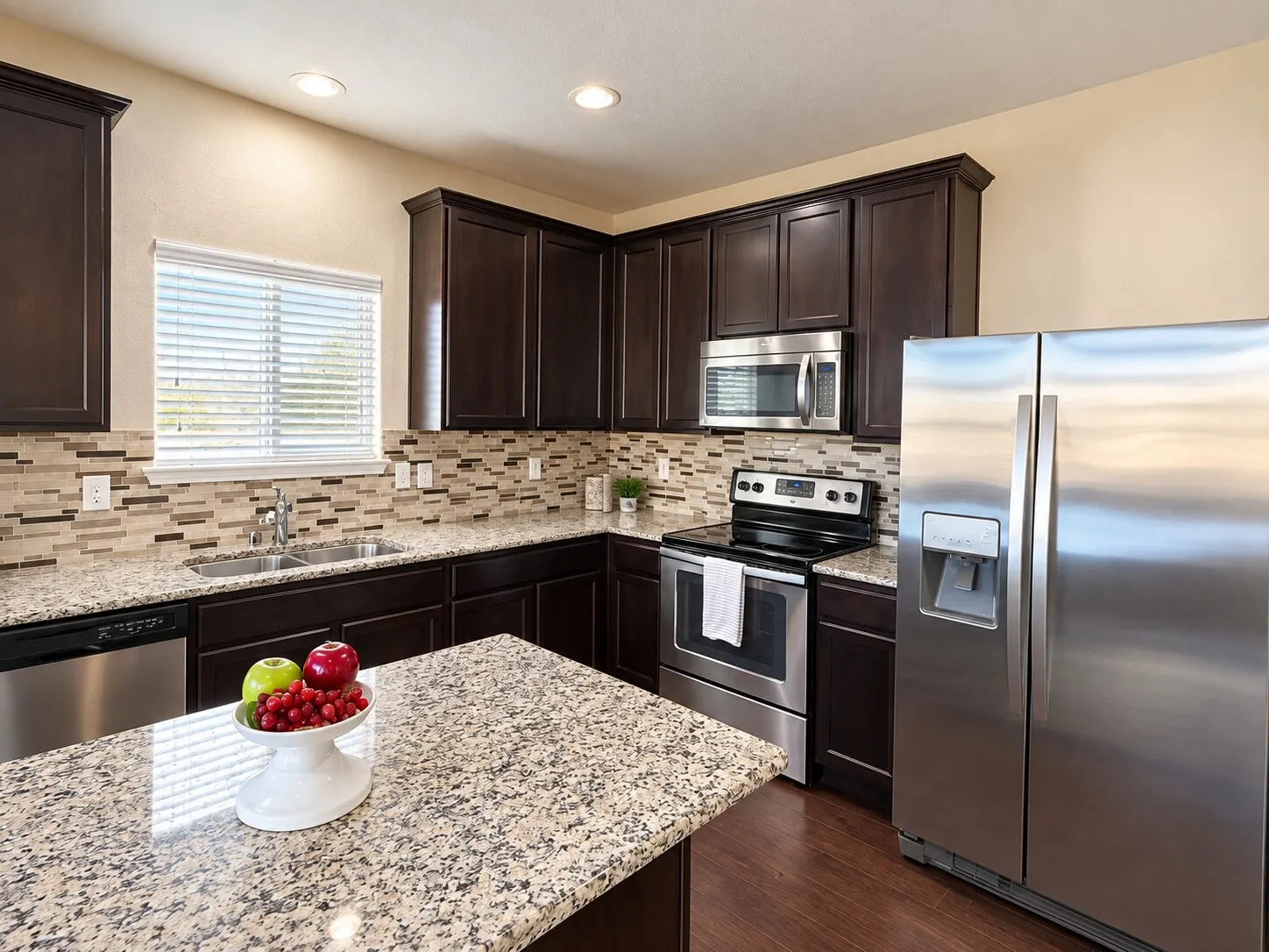 Dark wood cabinetry, stainless steel appliances, granite countertops, mosaic tile backsplash, and recessed lighting