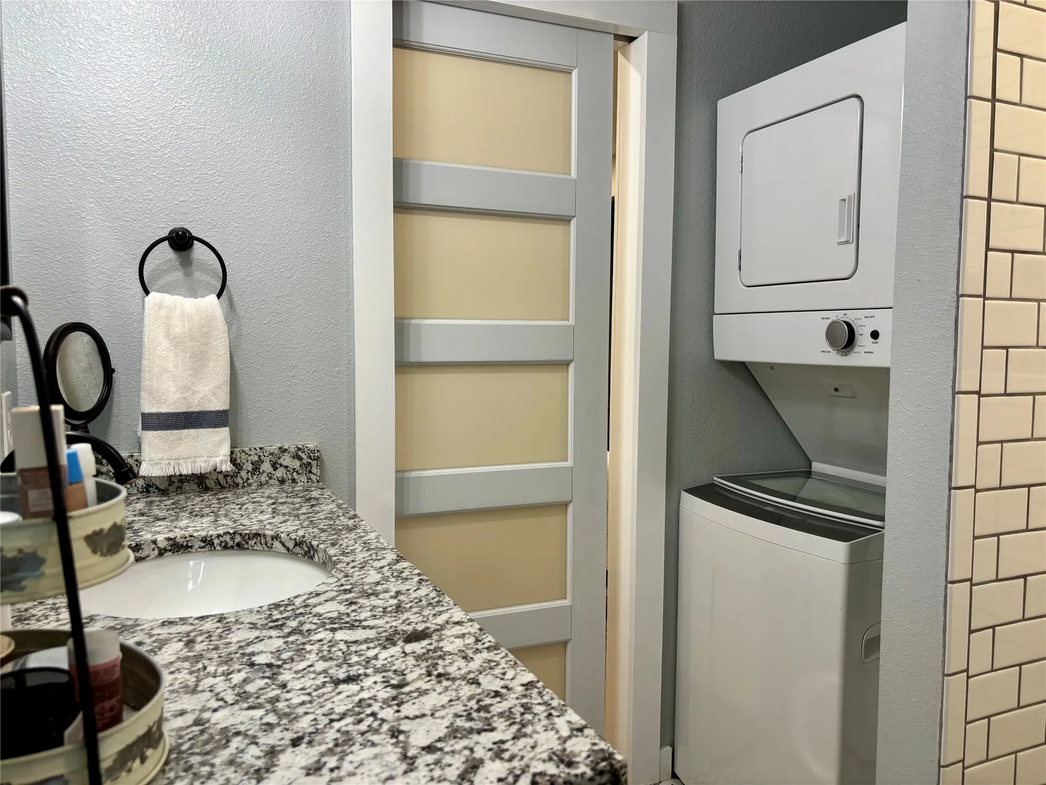 Bathroom vanity with a granite countertop and undermount sink. Tthe sliding pocket door separates the bathroom and bedroom. The subway tile to the right is the walk-in shower. The washer and drying convey with the home.