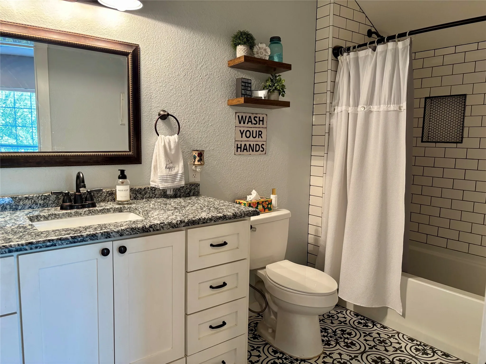 Bathroom featuring a single vanity with stone countertop, white shaker-style cabinetry, and a shower-over-tub with subway tile surround