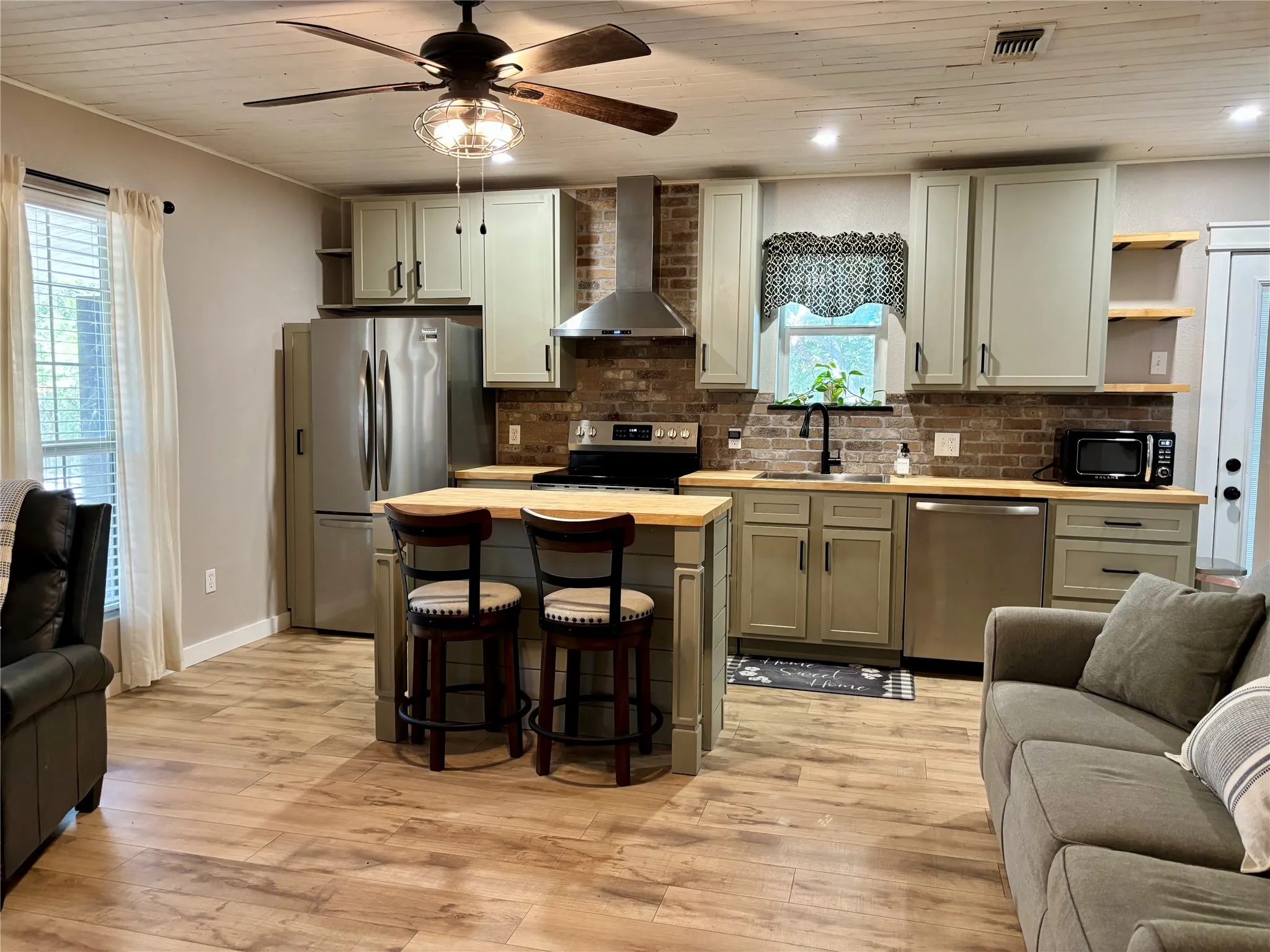 Kitchen featuring wood-finish flooring, a central island with seating, brick backsplash, stainless steel appliances, and a wood-slat ceiling.