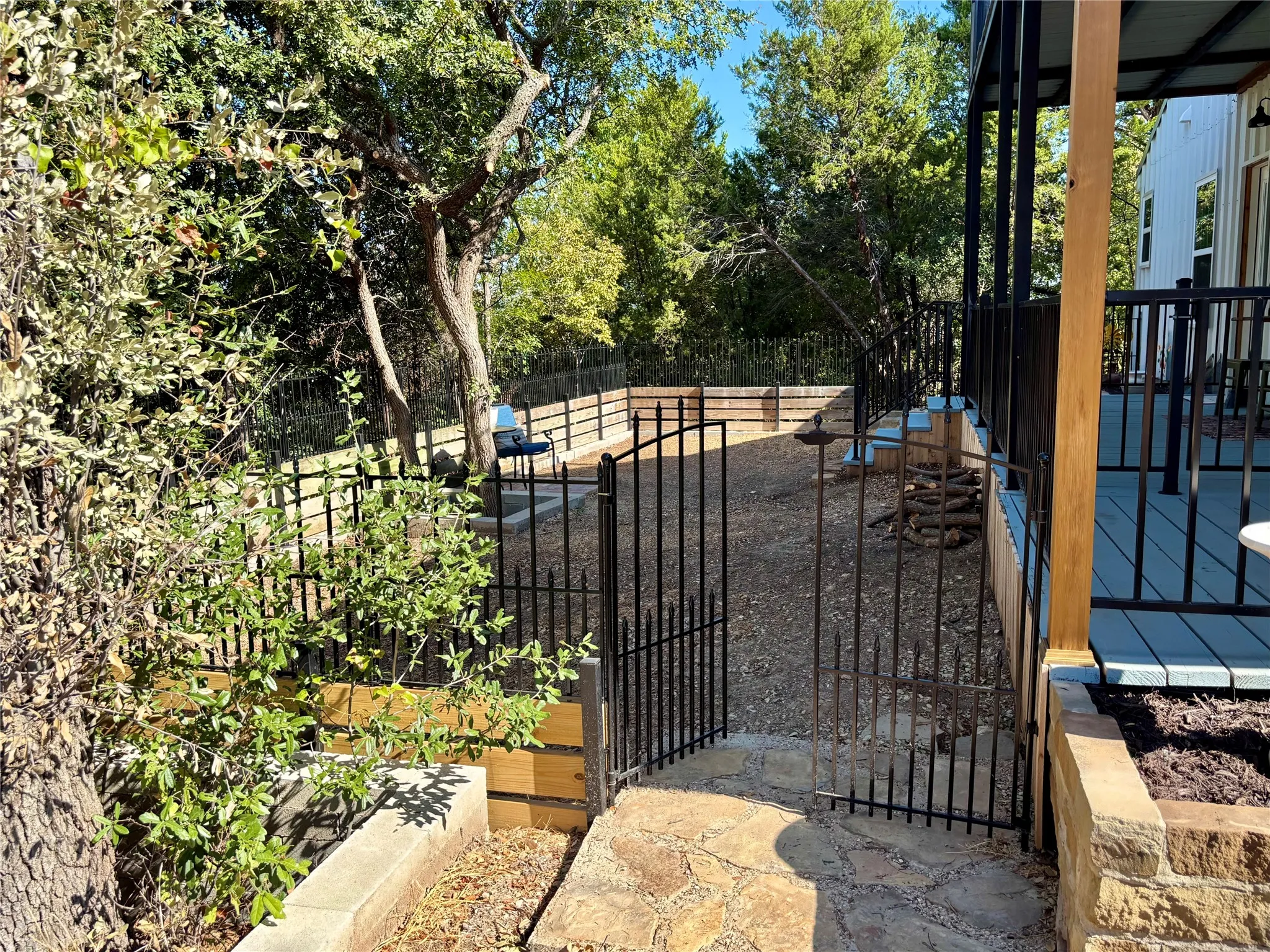 Gated sideyard area featuring flagstone steps, tiered landscaping, and a composite deck with black metal railing