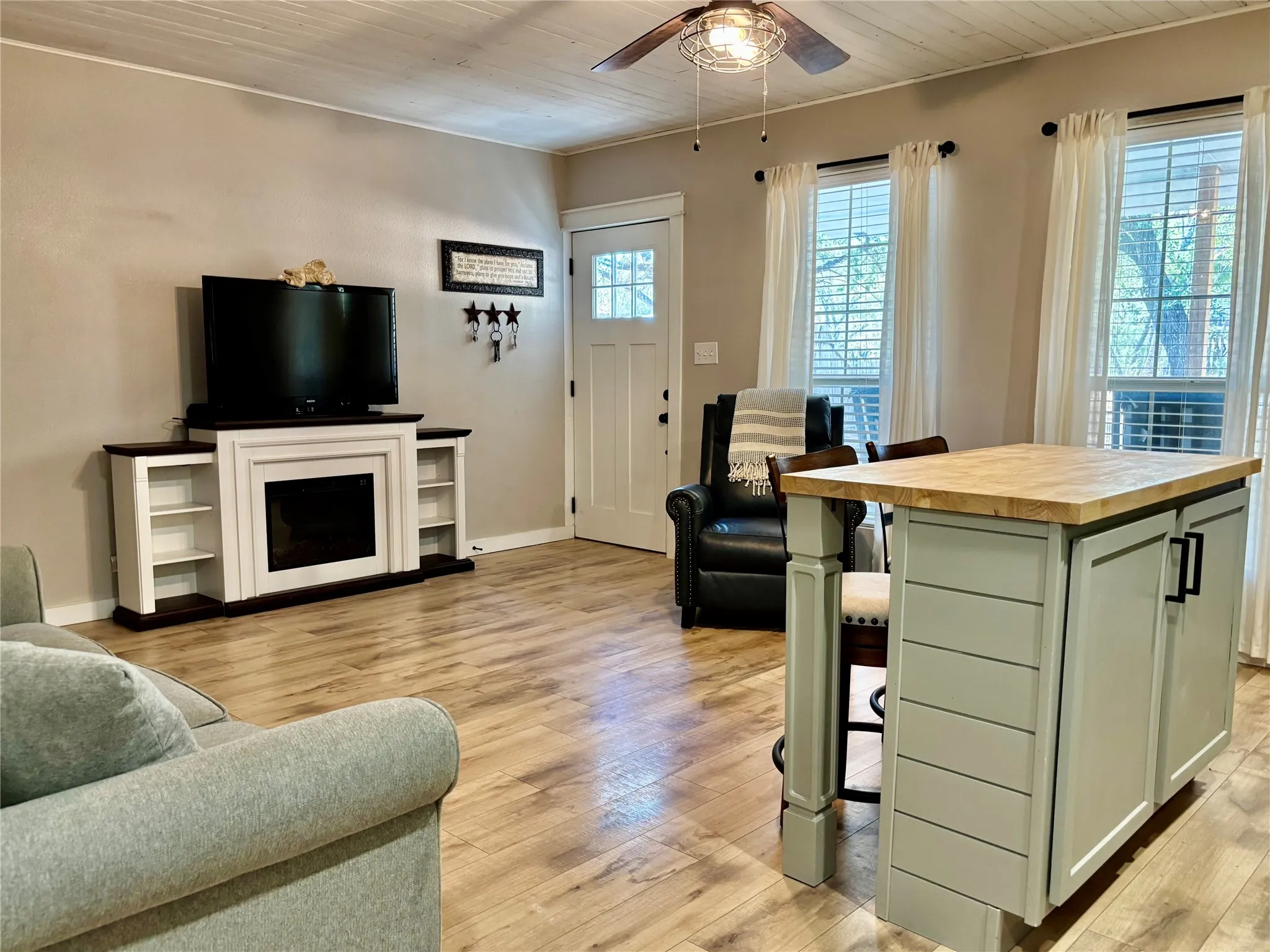 Front door entrance, wood-finish flooring throughout, ceiling fan, a shiplap ceiling, natural lighting, and a kitchen island.