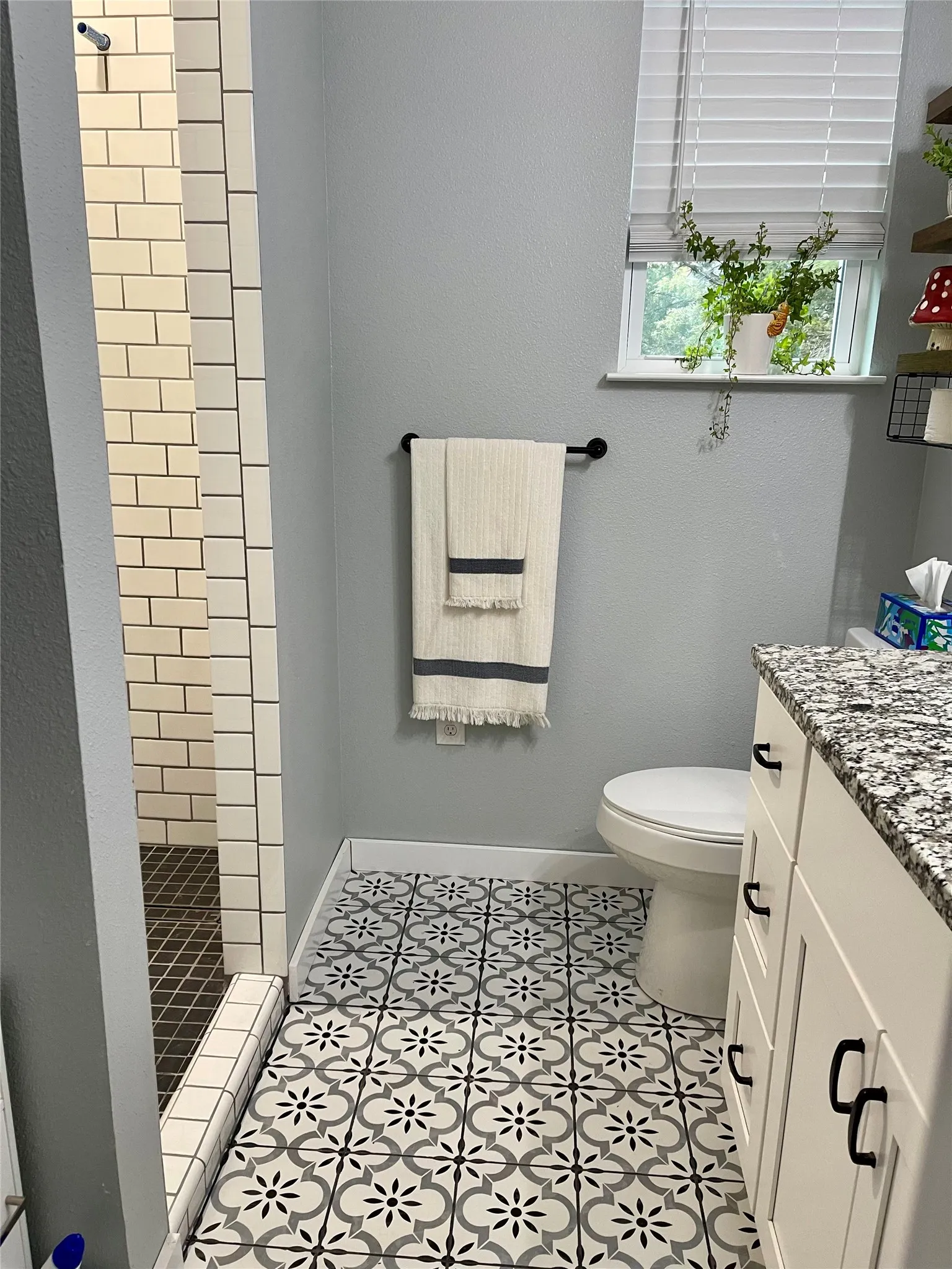 Patterned floor tile, white shaker-style cabinetry, dark hardware accents, and subway tile shower
