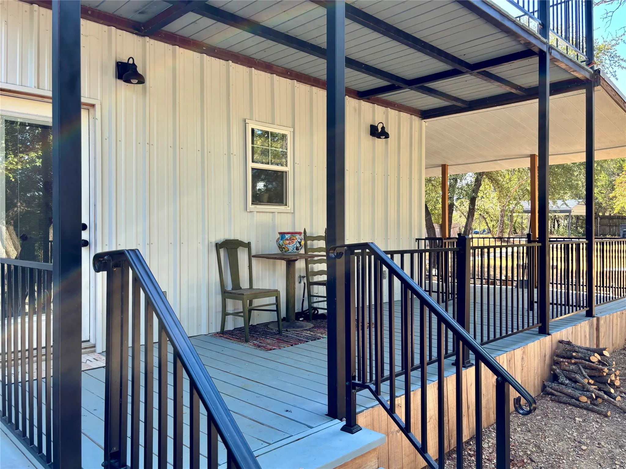 Covered porch with black metal railings. The door leads into the kitchen, the stairs lead into the fenced side yard and the porch wraps around to the front of the house.