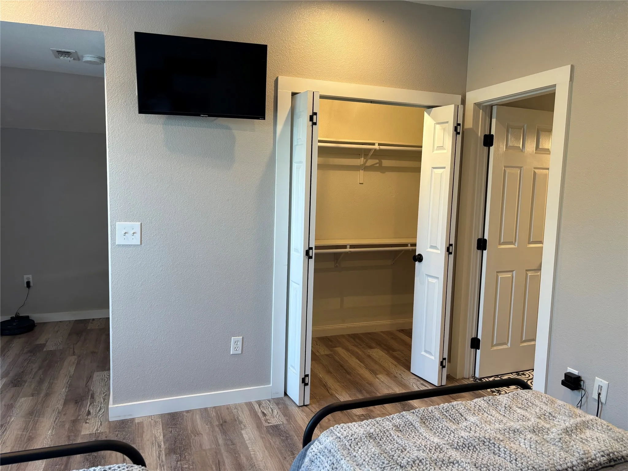 Wood-finish flooring throughout, white trim, and a built-in closet with shelving. The door to the right leads to the bathroom. The open area to the left leads to the stairs. The TV conveys with the house.