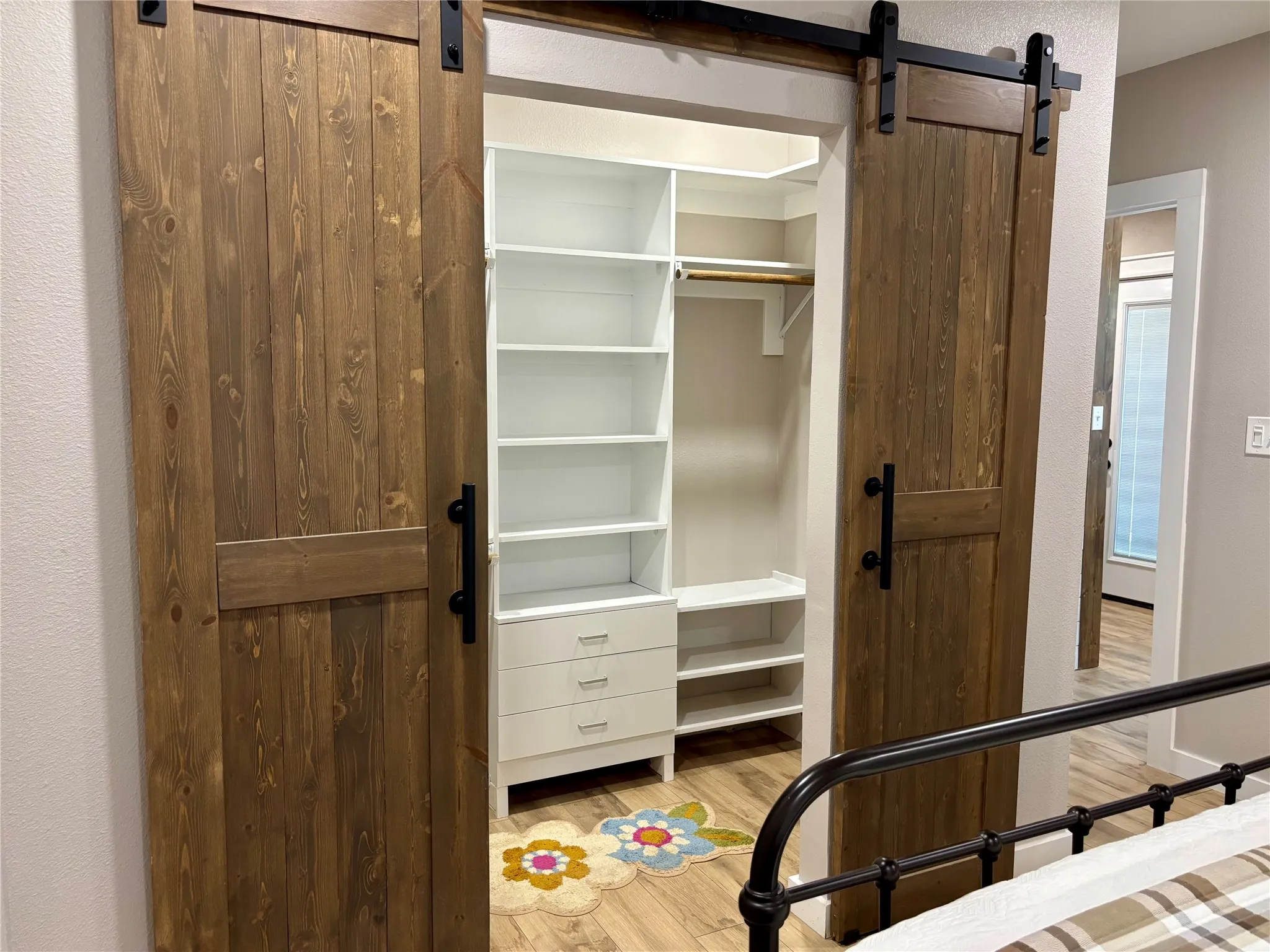 Custom wood barn doors with matte black hardware, built-in closet organization system, white shelving, and wood-finish flooring