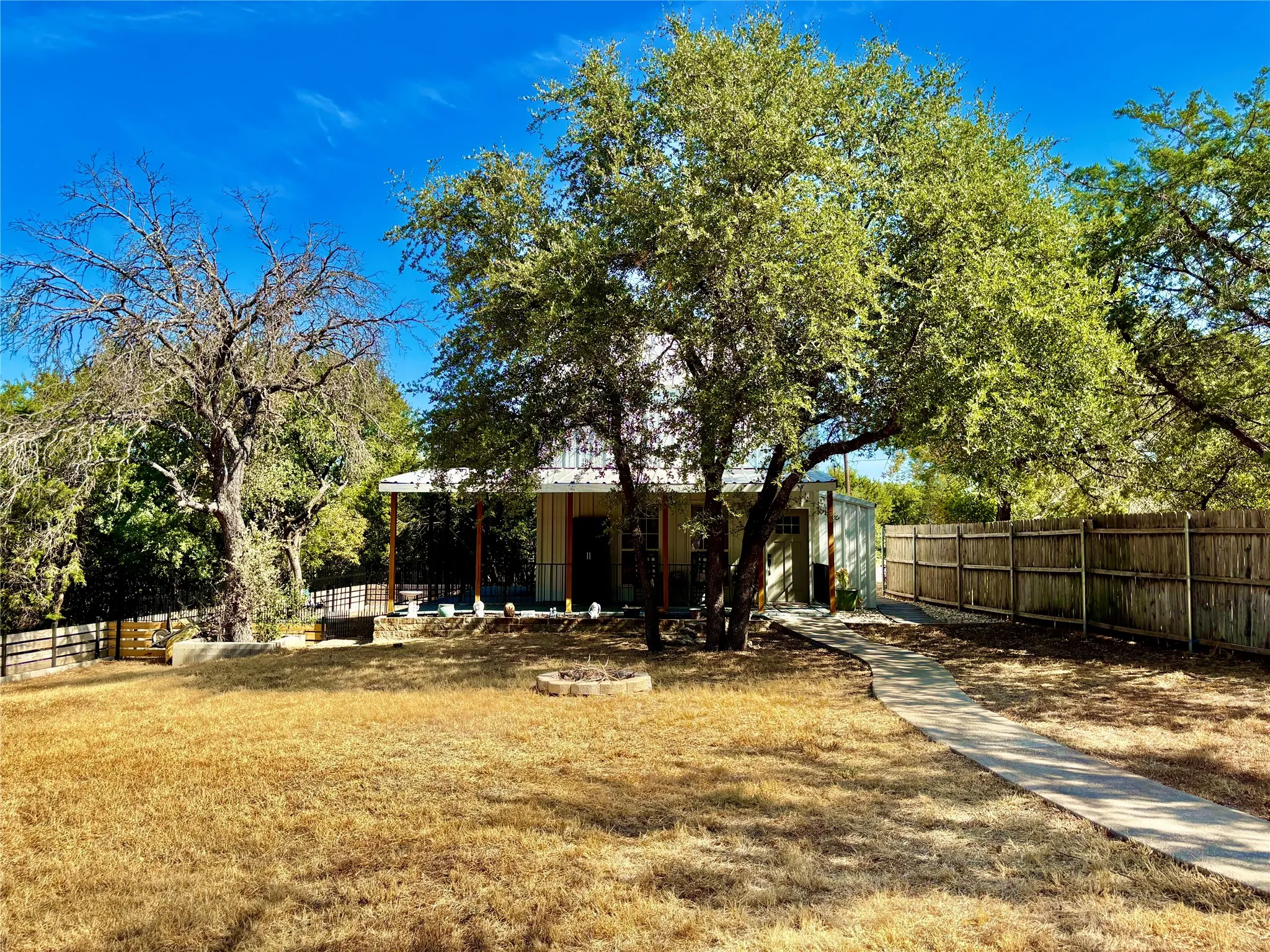 Exterior view of 111 Rupert Ct. featuring covered porch, mature trees, a privacy fence, and a concrete path from the carport to the home.
