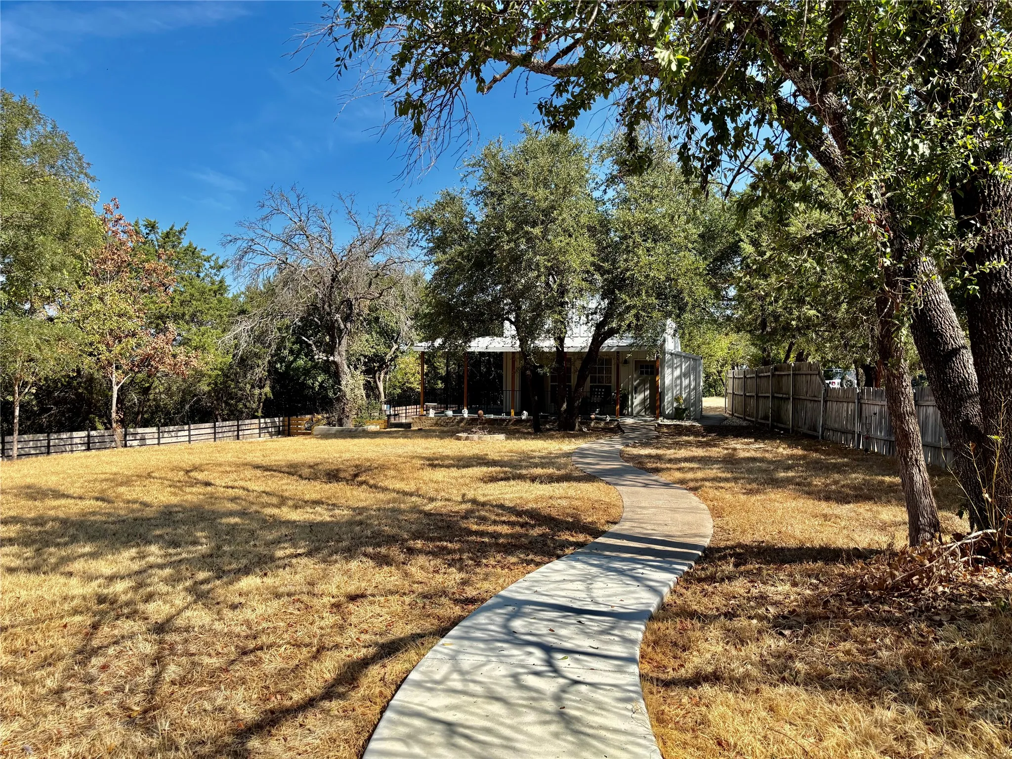 Expansive front yard with a curved concrete pathway, mature trees, and a perimeter fence. The property extends further to the left. Total acreage is just over a 1/2 acre.