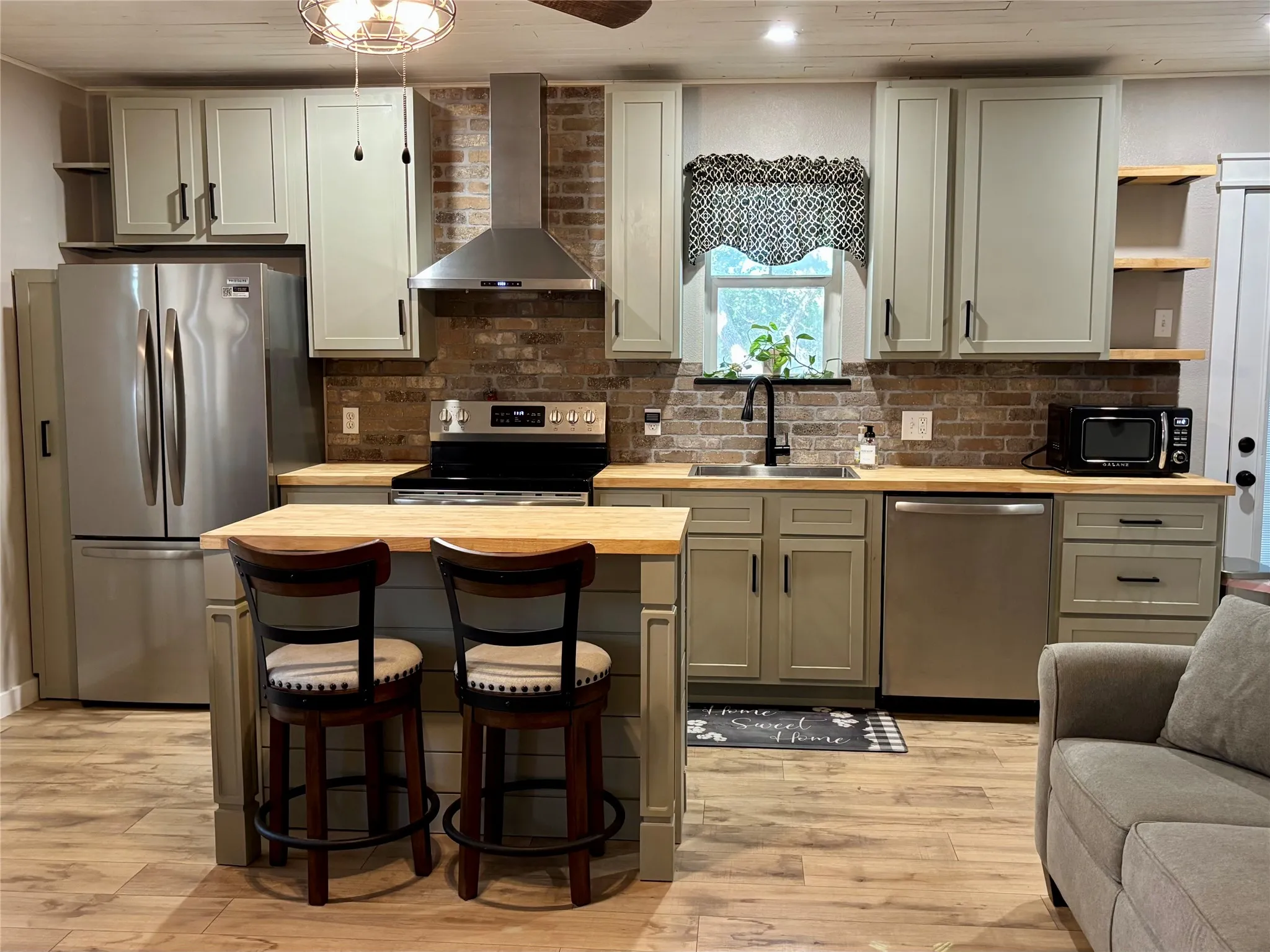 Kitchen featuring stainless steel appliances, wood-finish flooring, brick backsplash, and an island with a wood countertop. The refrigerator conveys with the home