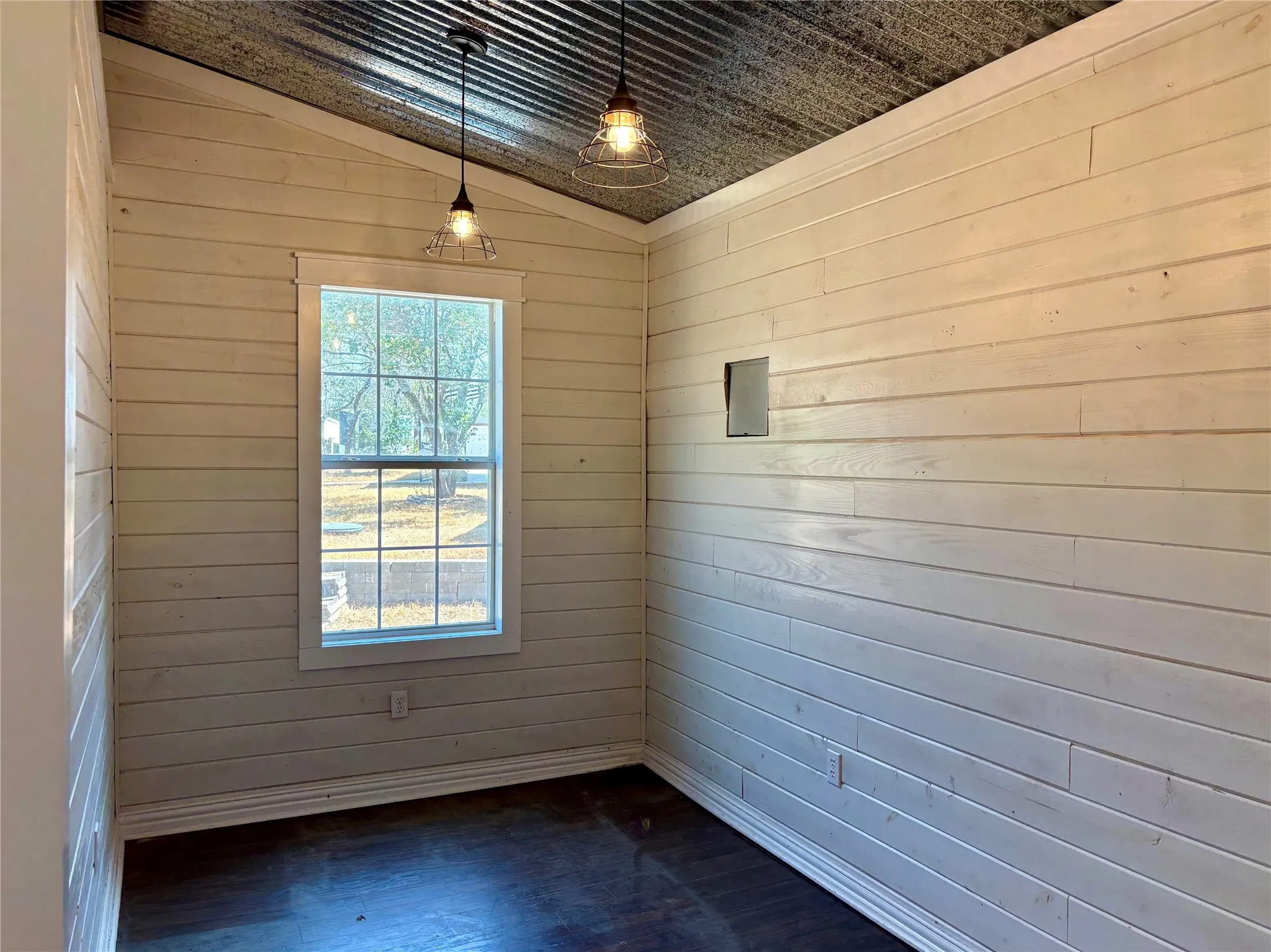 Inside look at the She / He Shed. Vaulted ceiling with corrugated metal finish, shiplap walls, dark wood-finish flooring, and industrial-style pendant lighting