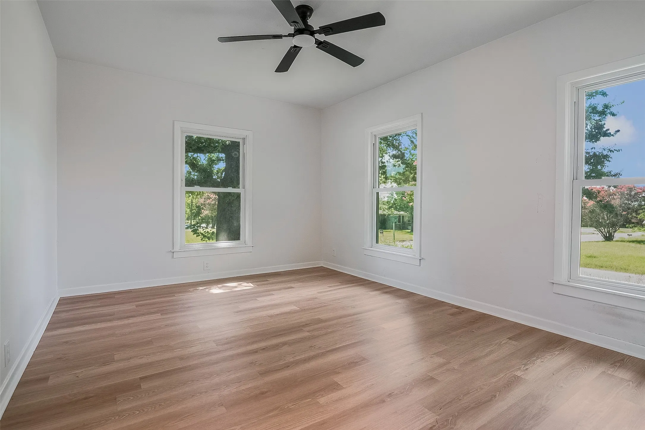Wood-finish flooring, white walls, multiple windows, and a ceiling fan