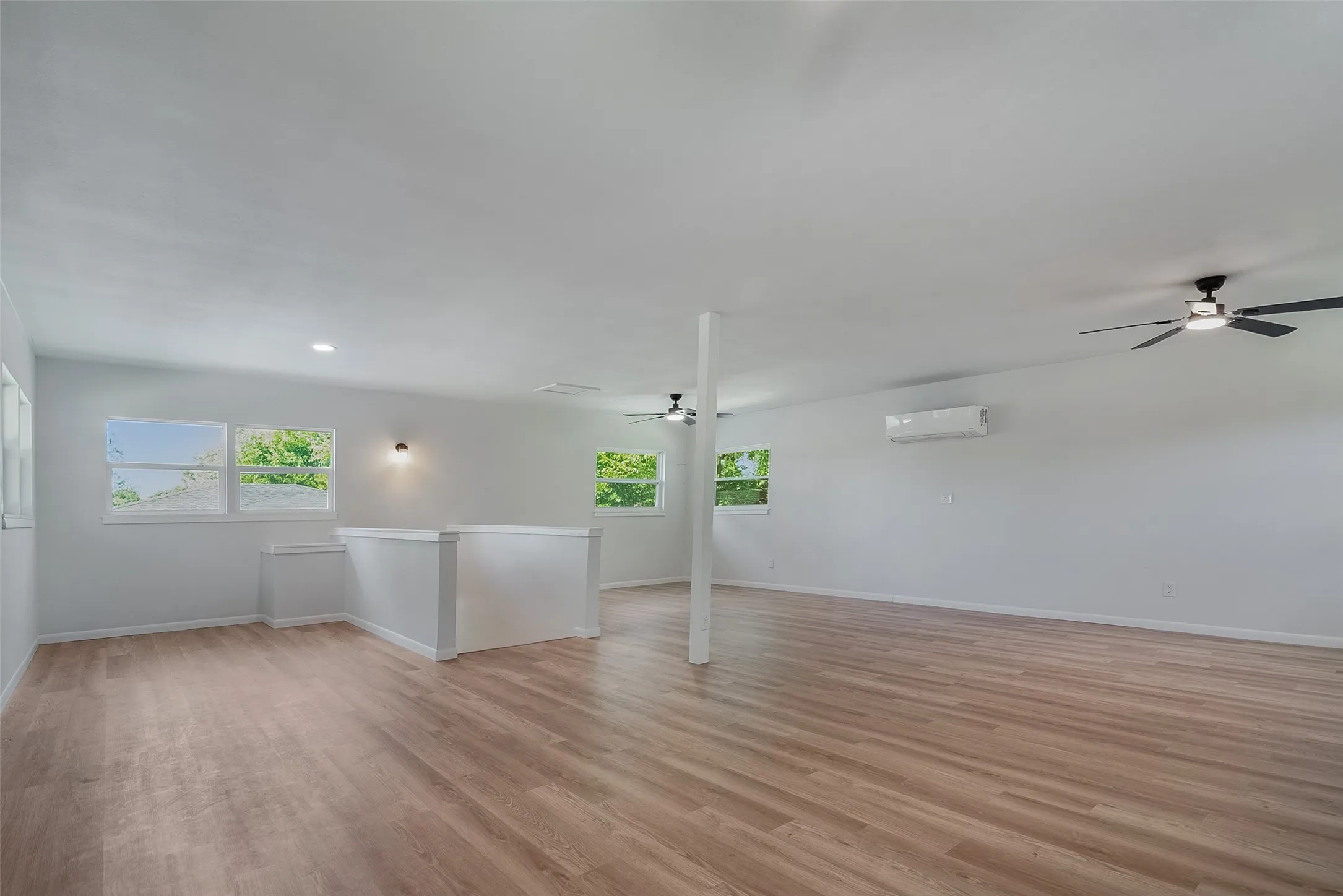 Expansive open space featuring light wood-finish flooring, multiple windows, and recessed lighting
