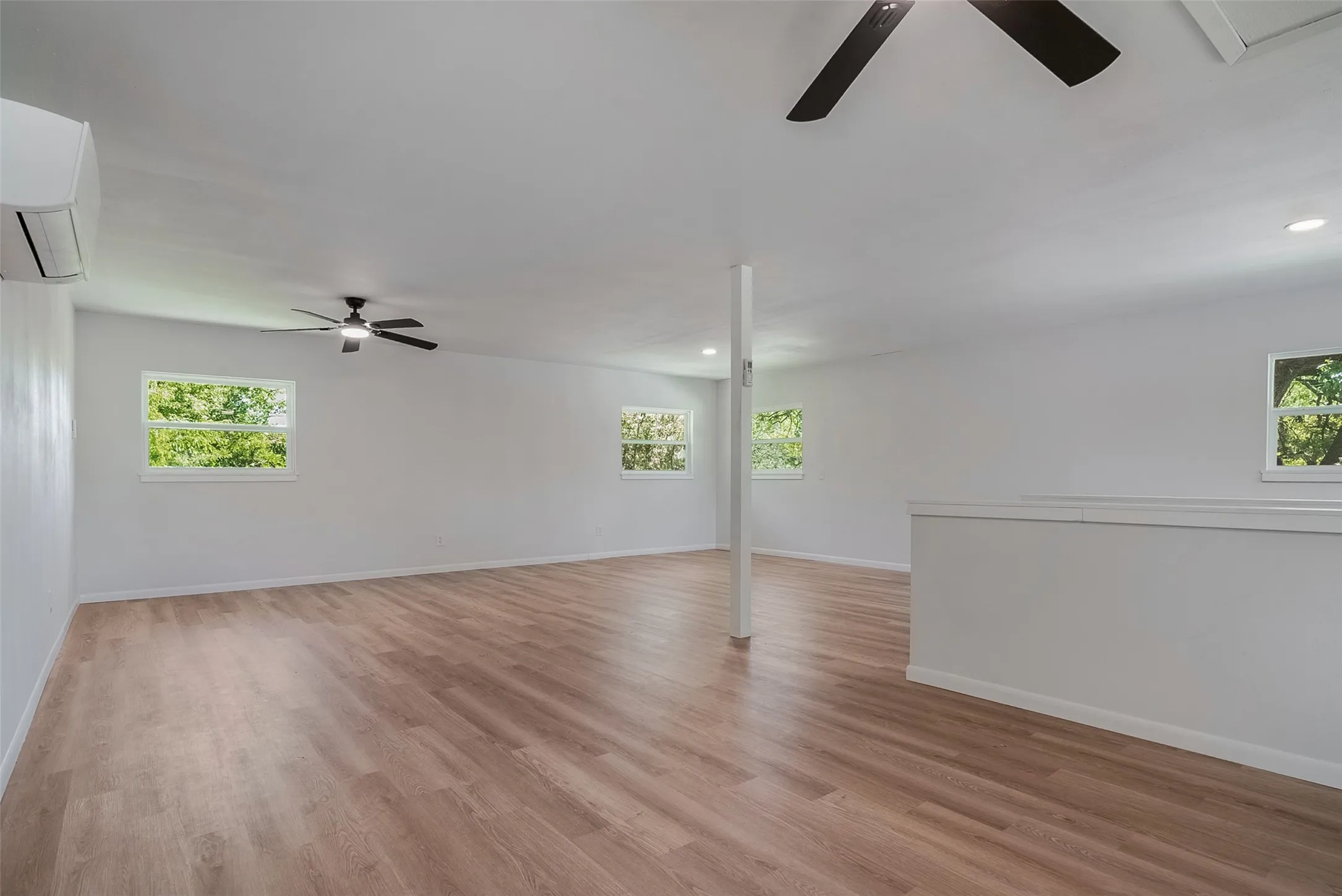 Spacious room featuring wood-finish flooring, white walls, multiple windows, and ceiling fans