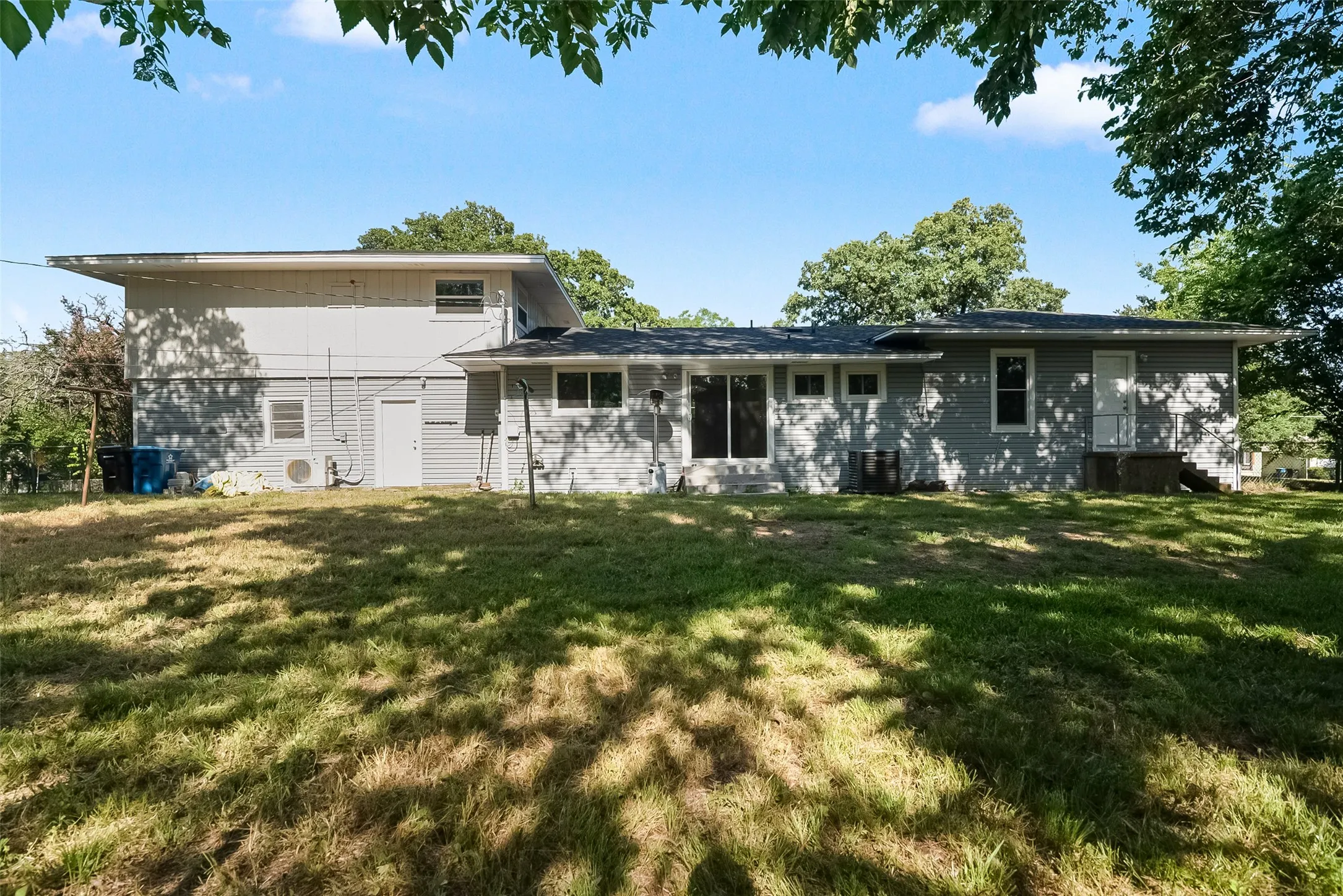 Rear exterior with light gray siding, multiple windows, and a dark shingle roof