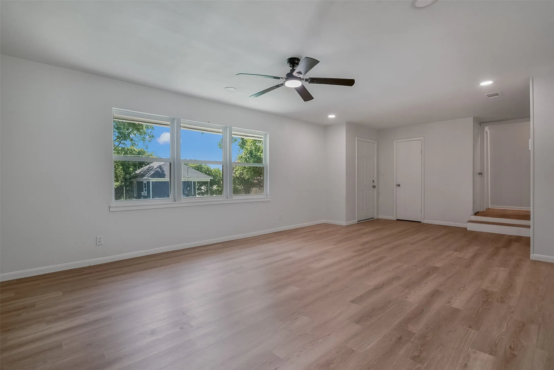 Spacious room featuring wood-finish flooring, a contemporary ceiling fan, and recessed lighting
