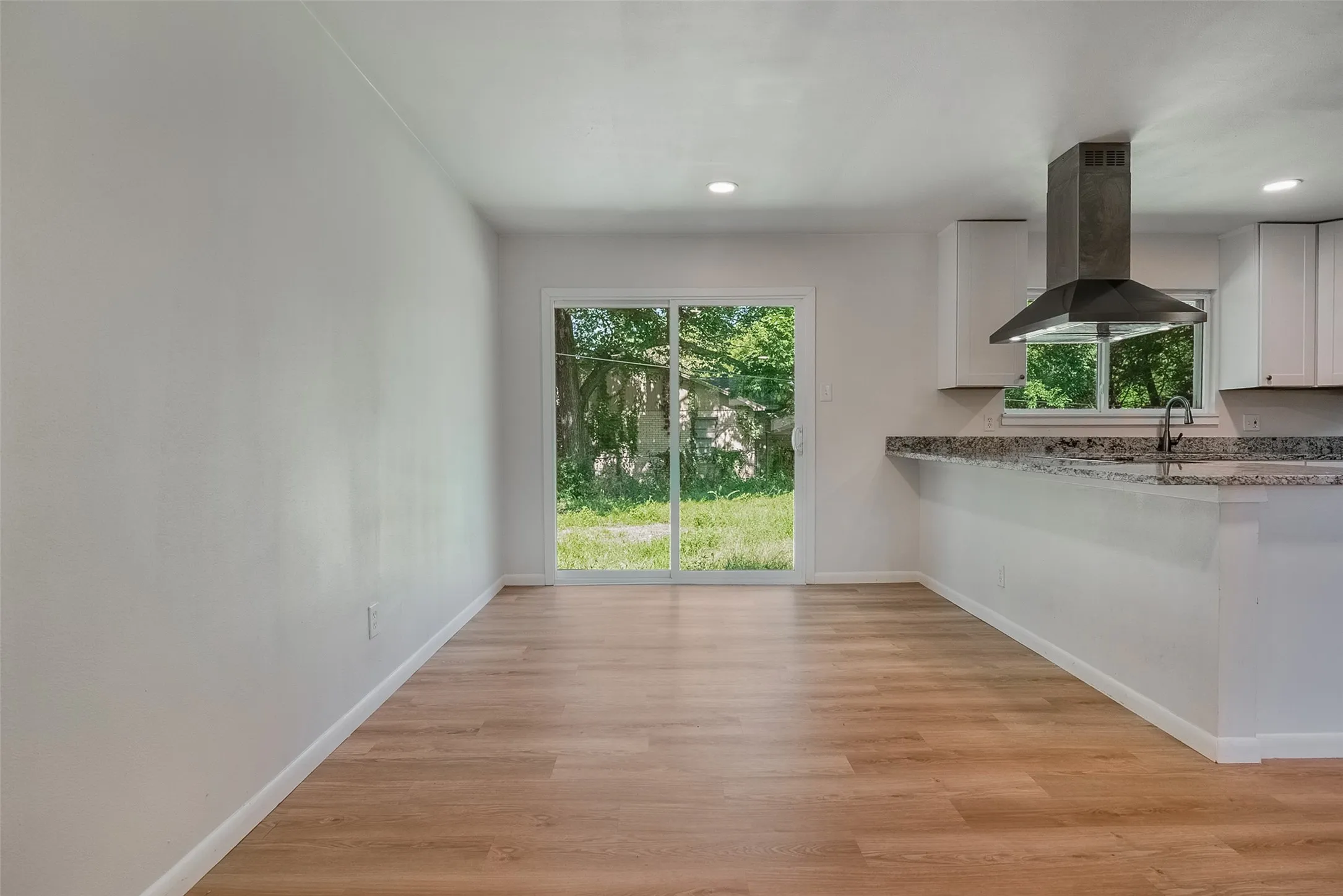 Wood-finish flooring throughout, recessed ceiling lighting, sliding glass door, white cabinetry, and a stainless steel range hood