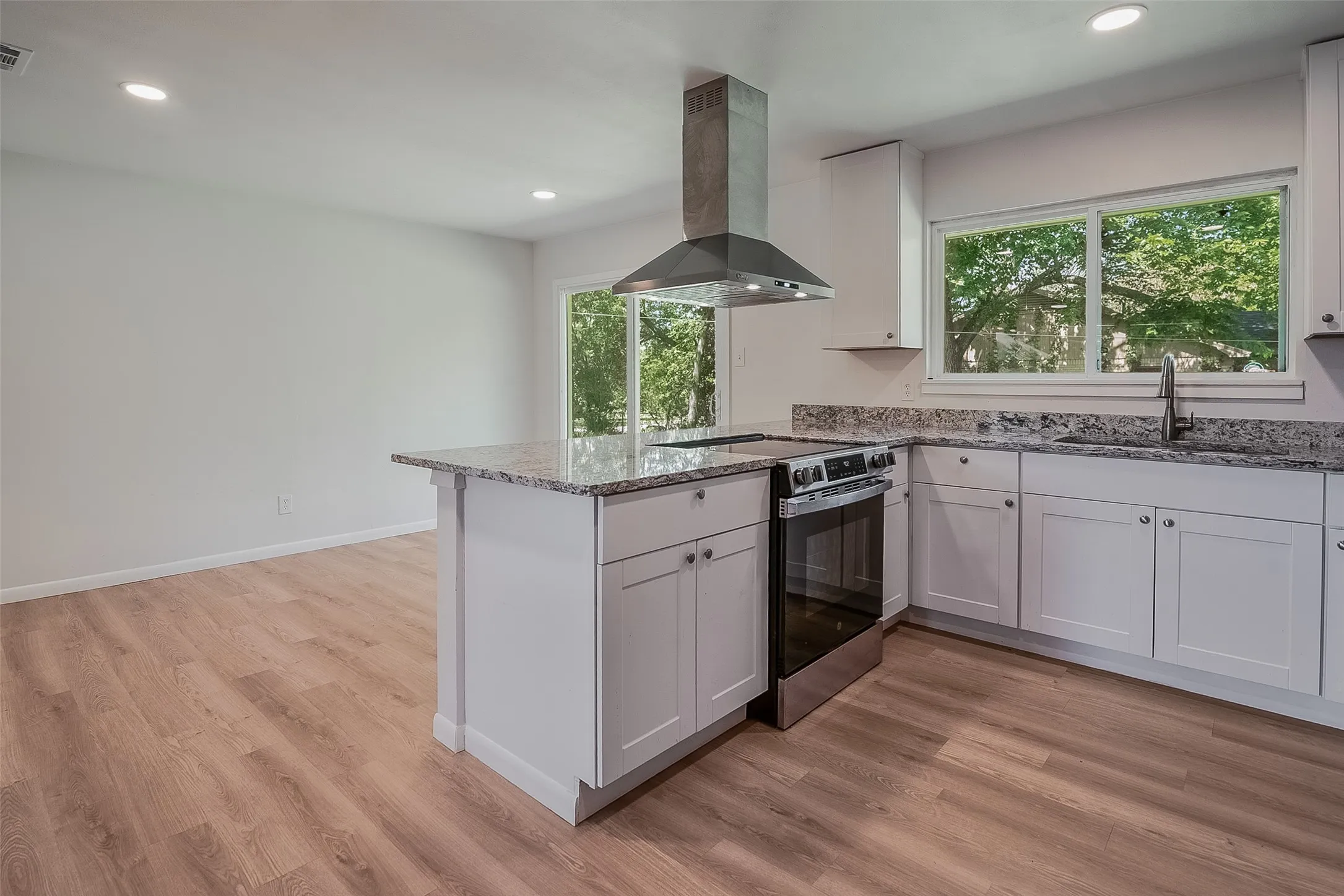 Kitchen featuring a central island, stainless steel range with overhead hood, white cabinetry, and light-toned wood-finish flooring