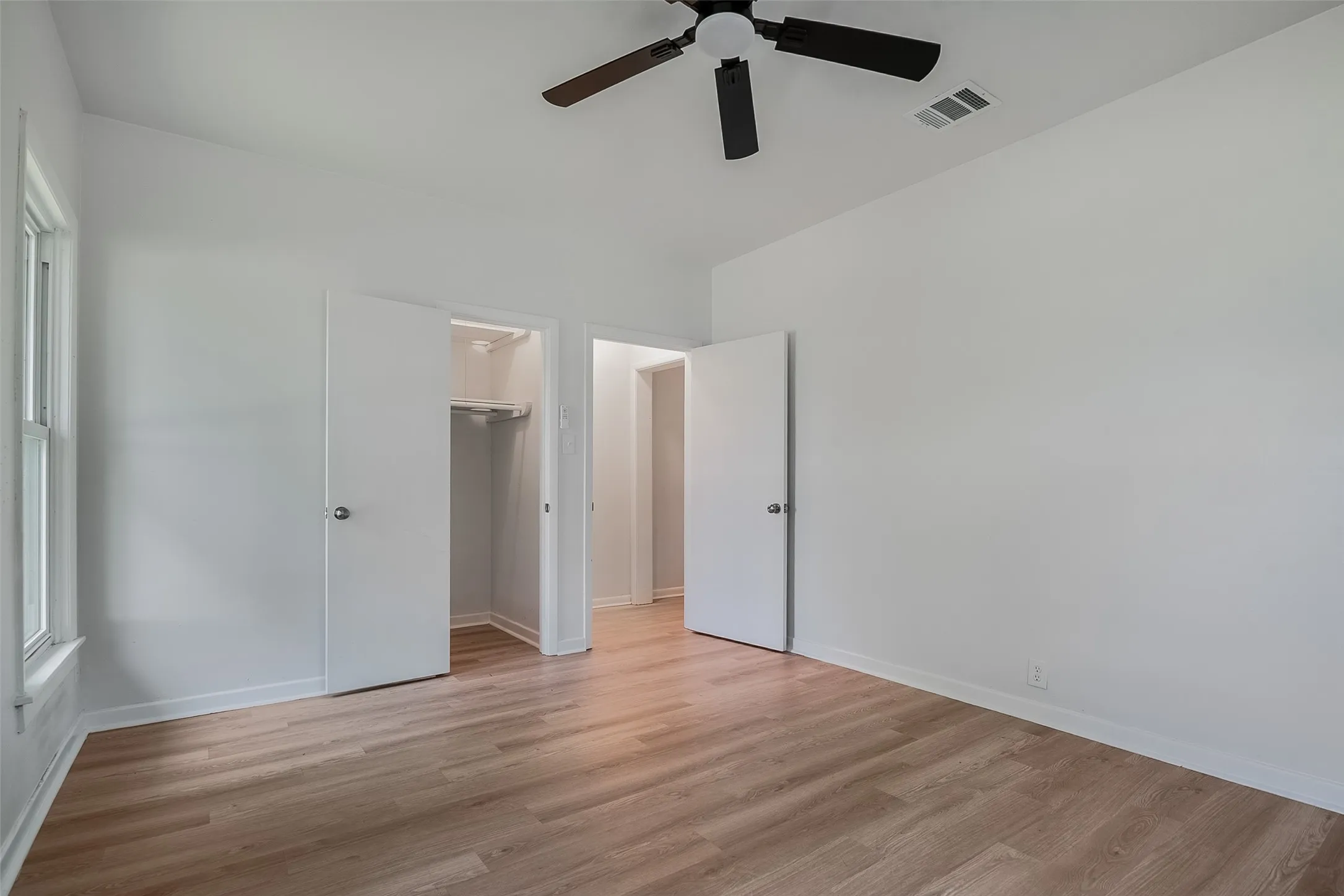Spacious room featuring wood-finish flooring, a ceiling fan, and built-in closet storage