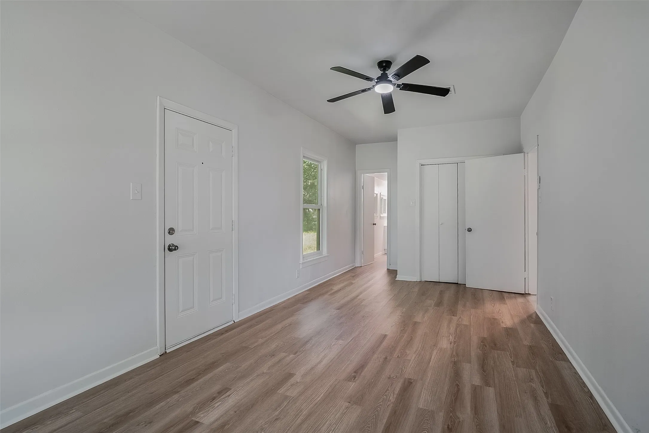 Wood-finish flooring, white walls, ceiling fan with light fixture, and white interior doors