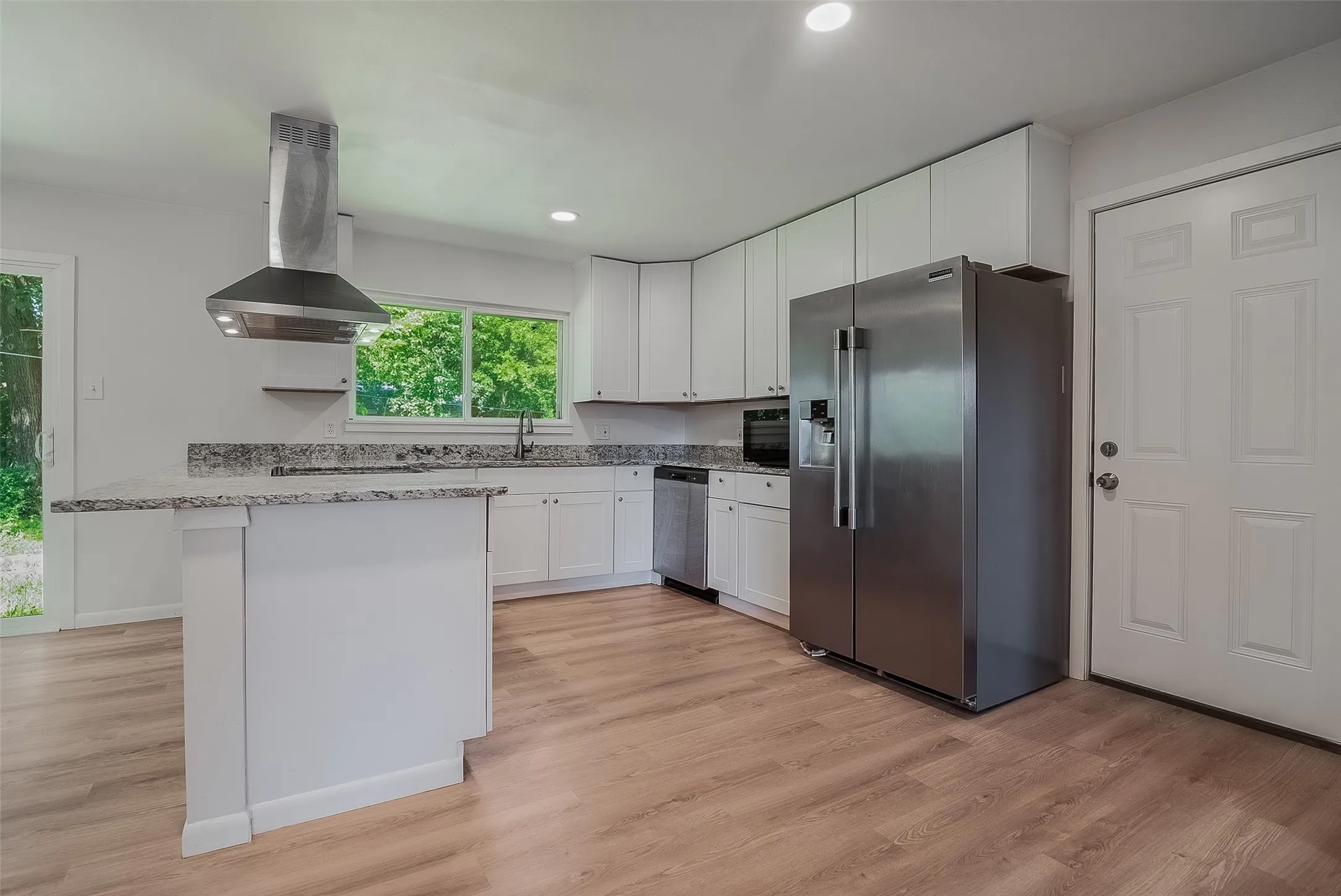 White shaker cabinetry, stainless steel appliances, wood-finish flooring, recessed lighting, and a granite-style countertop