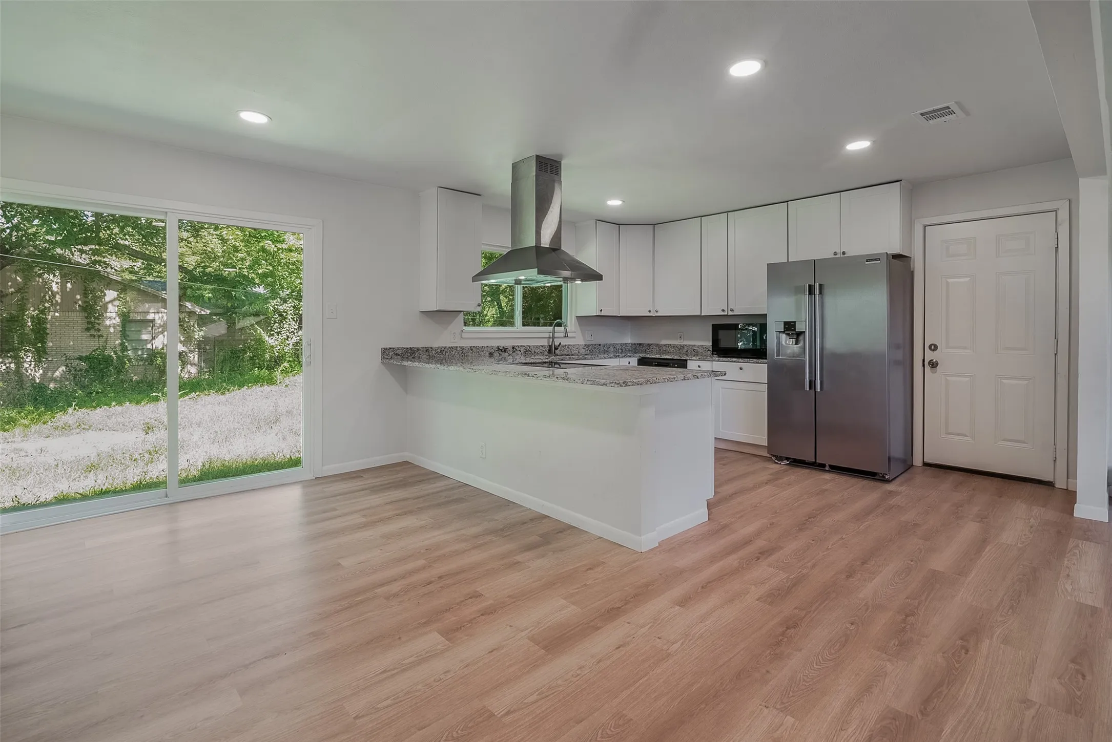 Open-concept kitchen with white cabinetry, stainless steel appliances, and a breakfast bar, complemented by wood-finish flooring and a sliding glass door
