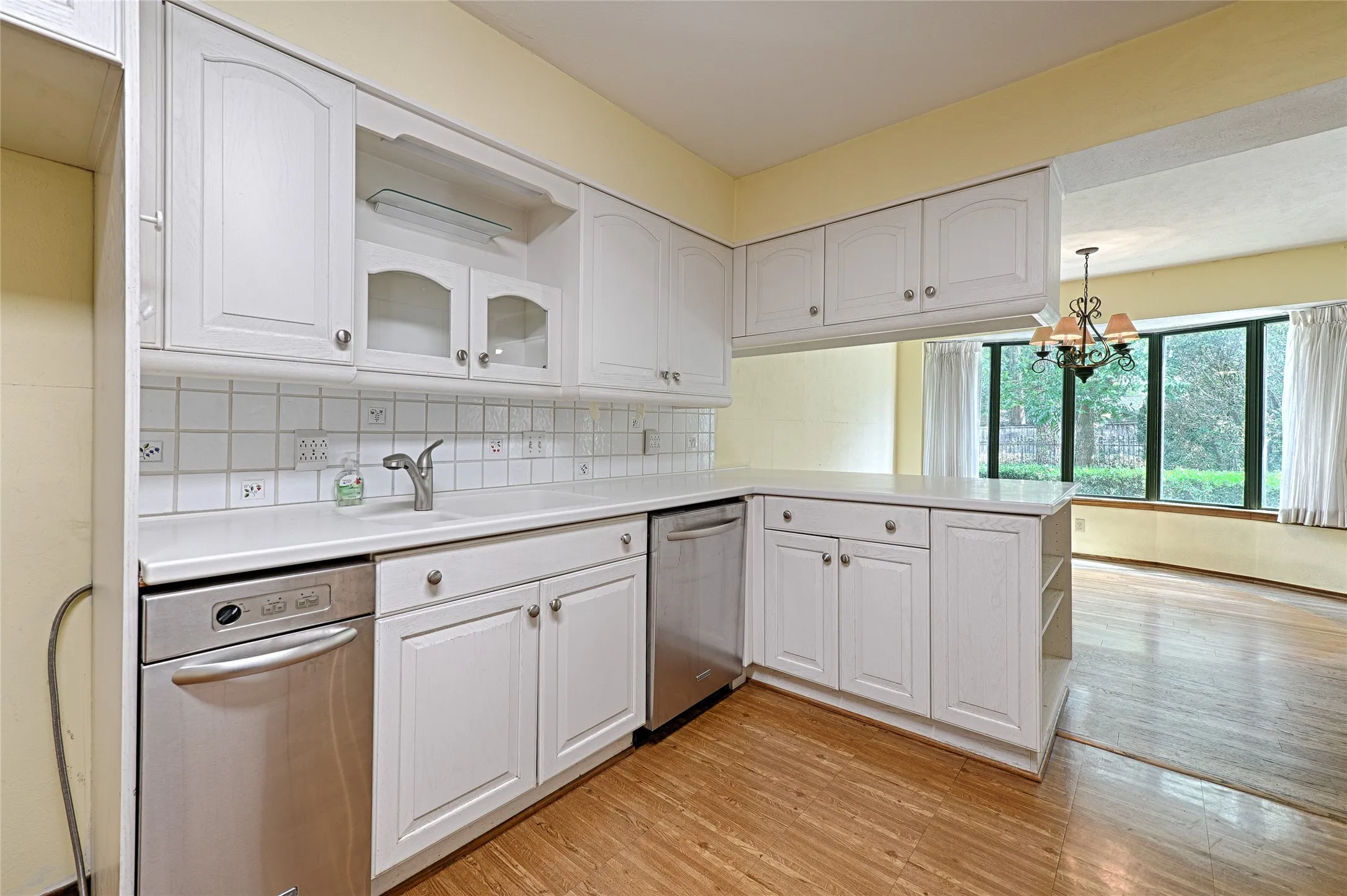 White cabinetry with brushed nickel hardware, white tile backsplash, stainless steel appliances, wood-finish flooring, and a chandelier