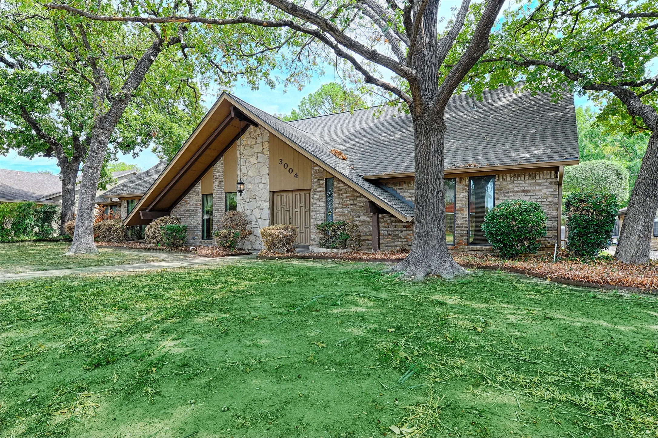 Pitched roofline with exposed eaves, stone facade detailing, brick exterior elements, and a sizable front lawn