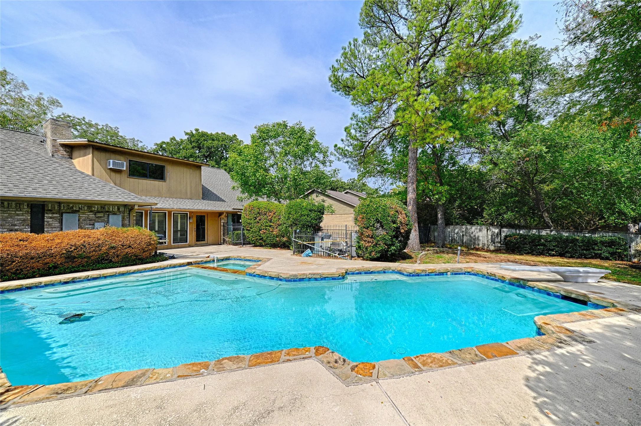 Expansive backyard featuring a custom-shaped swimming pool with stone coping, an integrated spa, and a concrete deck
