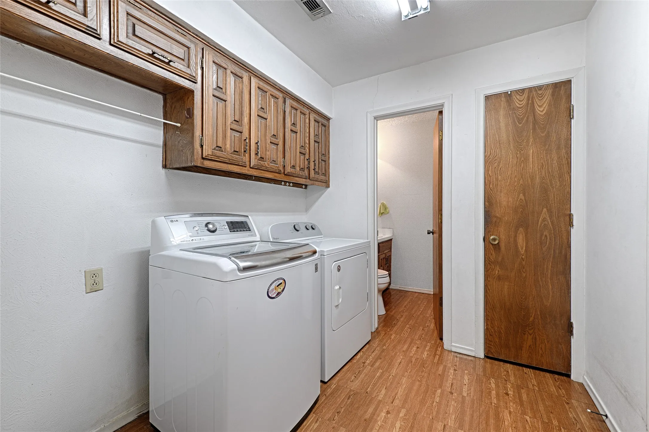 Laundry area featuring wood-finish flooring and upper cabinetry