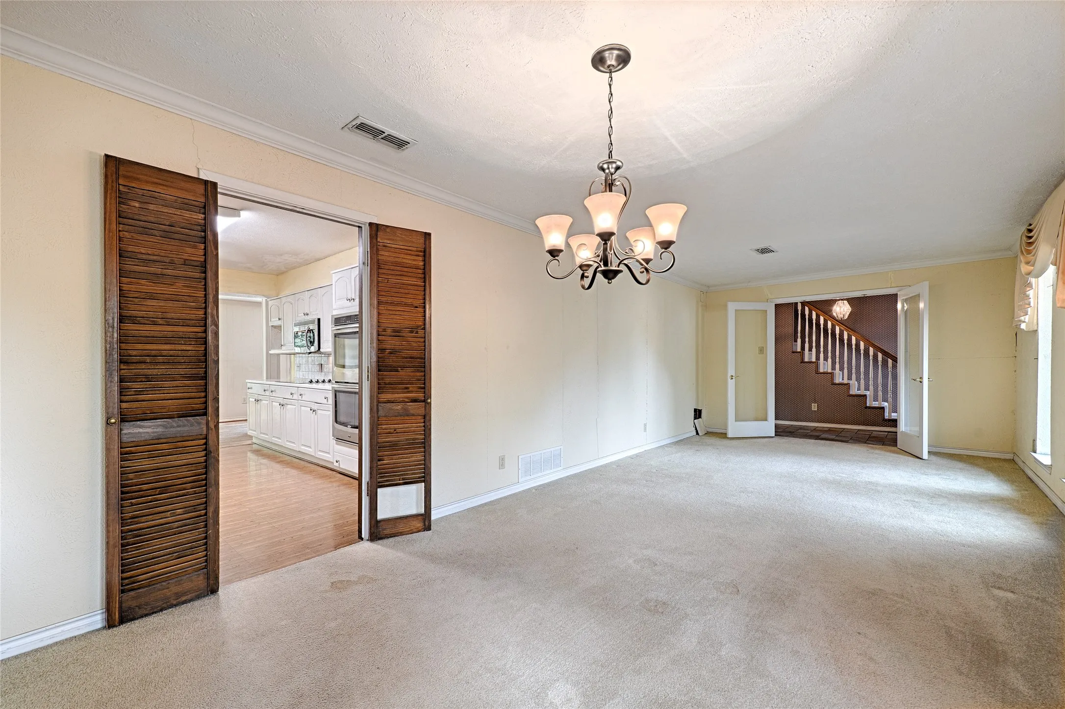 Carpeted main living area featuring a traditional chandelier, crown molding, and wooden louvered double doors