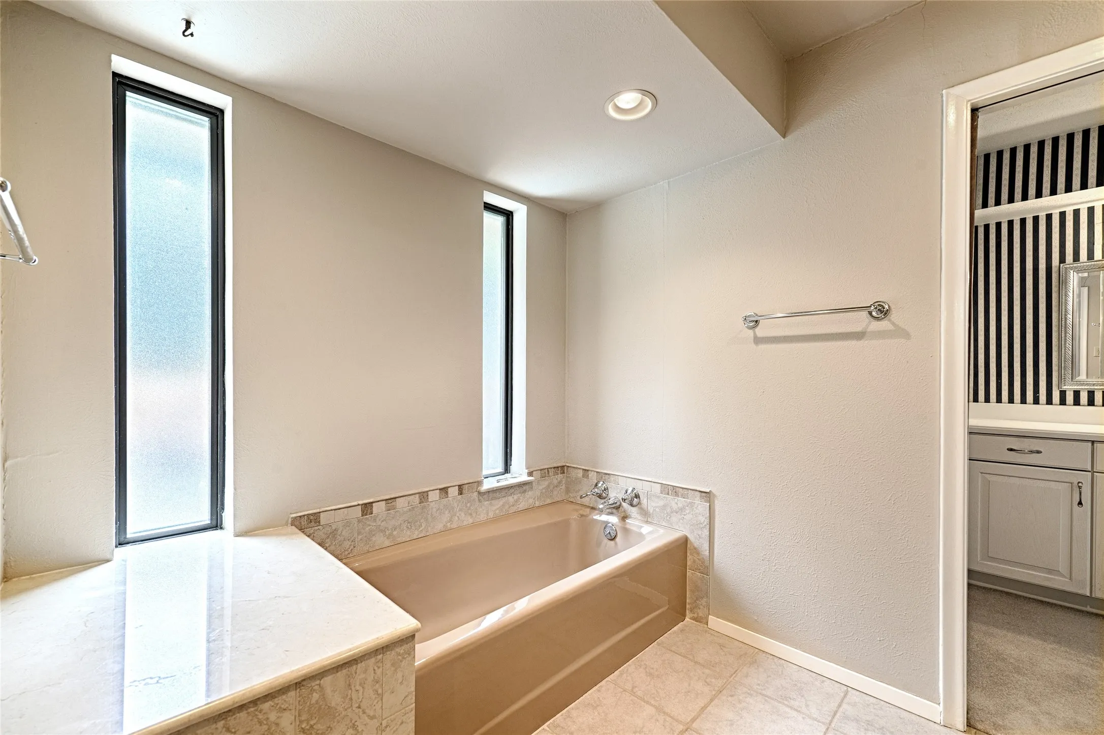 Built-in bathtub with tiled surround, light-colored tile flooring, and two frosted vertical windows