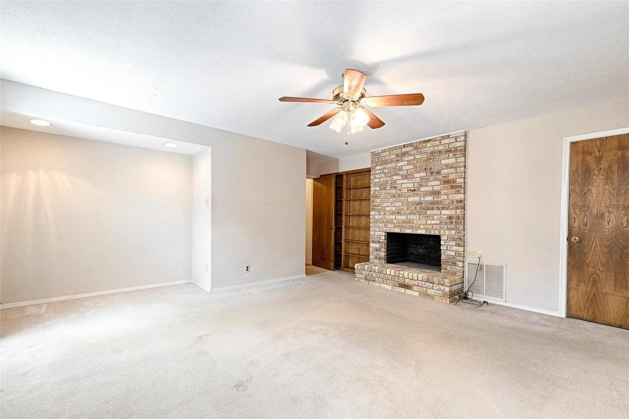 Spacious living area featuring a brick fireplace, built-in shelving, ceiling fan, and recessed lighting