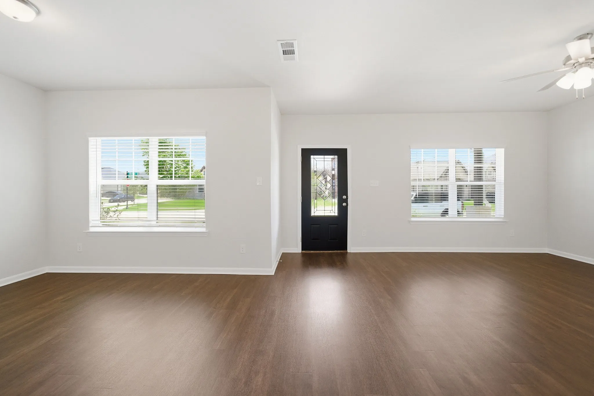 Expansive living area featuring wood-finish flooring, a ceiling fan, and multiple windows providing natural light