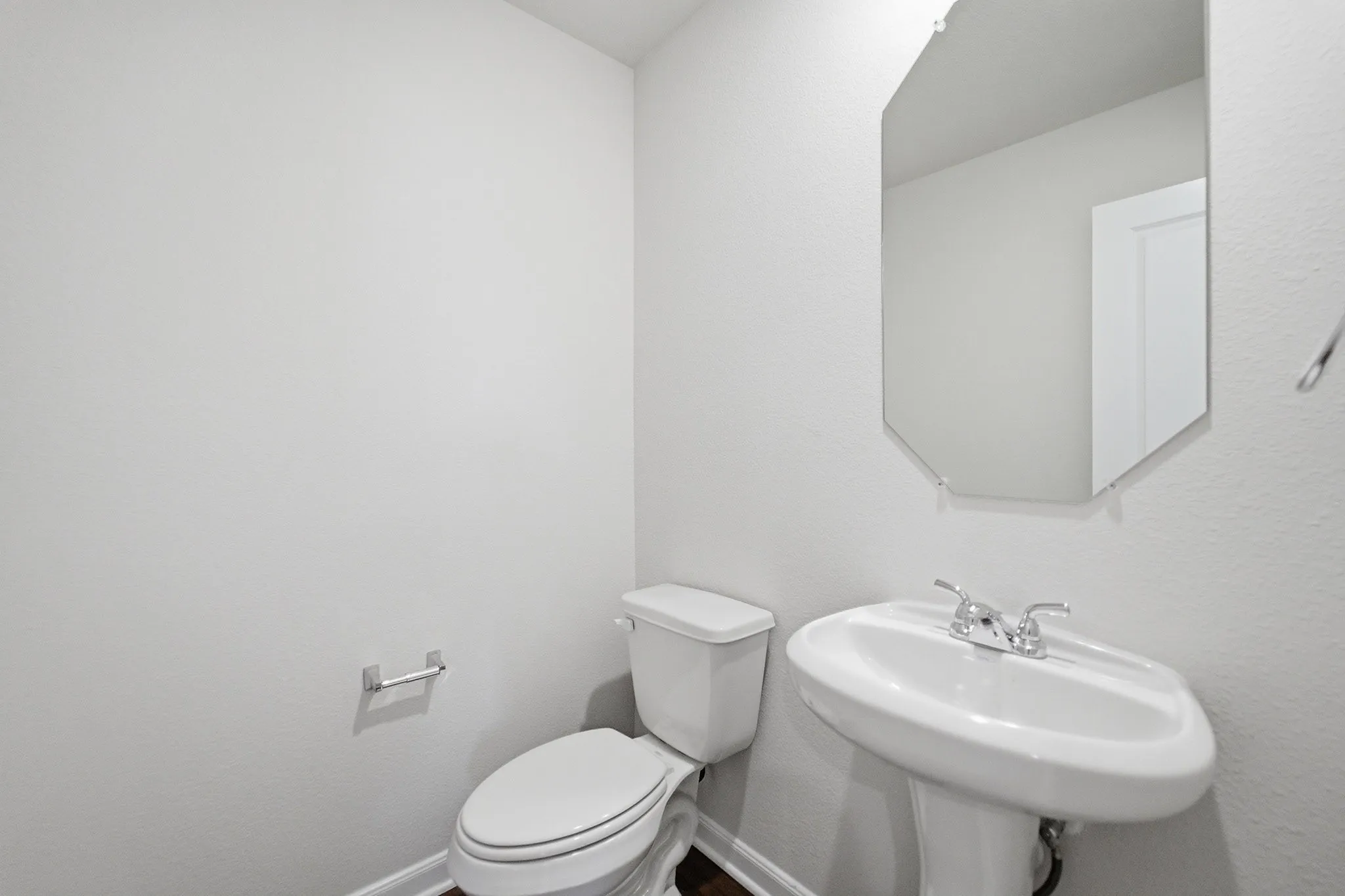 Pedestal sink with chrome faucet, white toilet, and octagonal wall mirror
