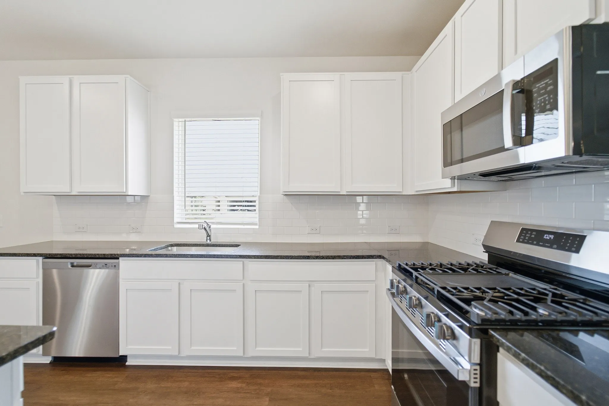 White shaker cabinetry, dark countertops, subway tile backsplash, stainless steel appliances, and wood-finish flooring