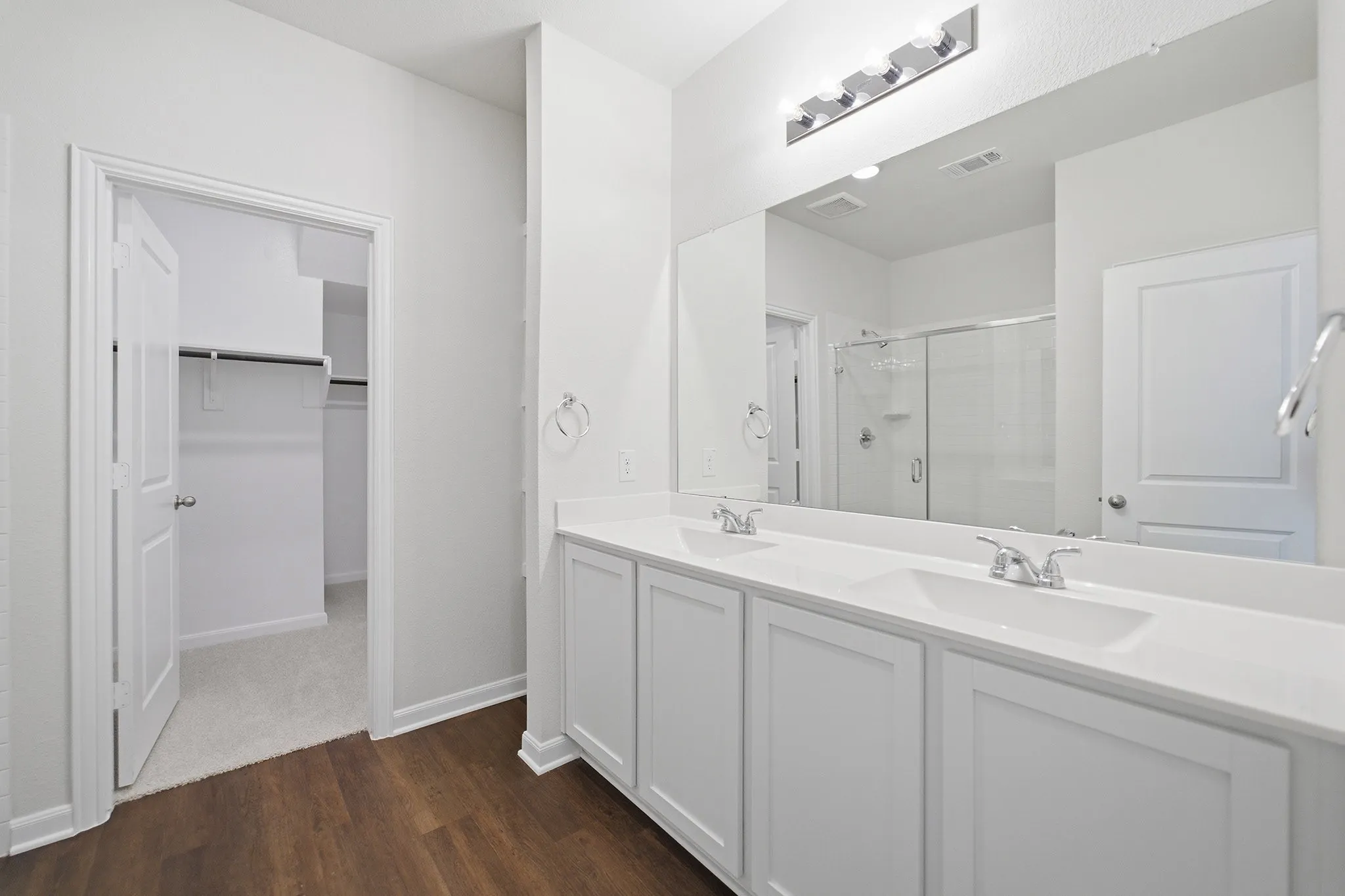 Dual vanity with integrated sinks, wood-finish flooring, a full-width mirror, and a built-in shower enclosure