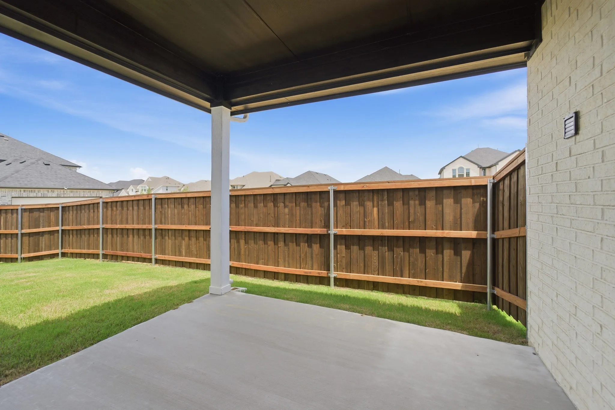 Covered patio with a concrete surface, expansive lawn, and wood privacy fencing