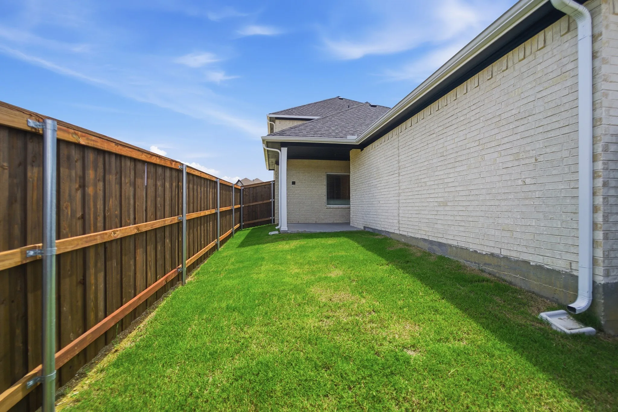 Spacious side yard featuring a privacy fence, lush lawn, and a brick exterior