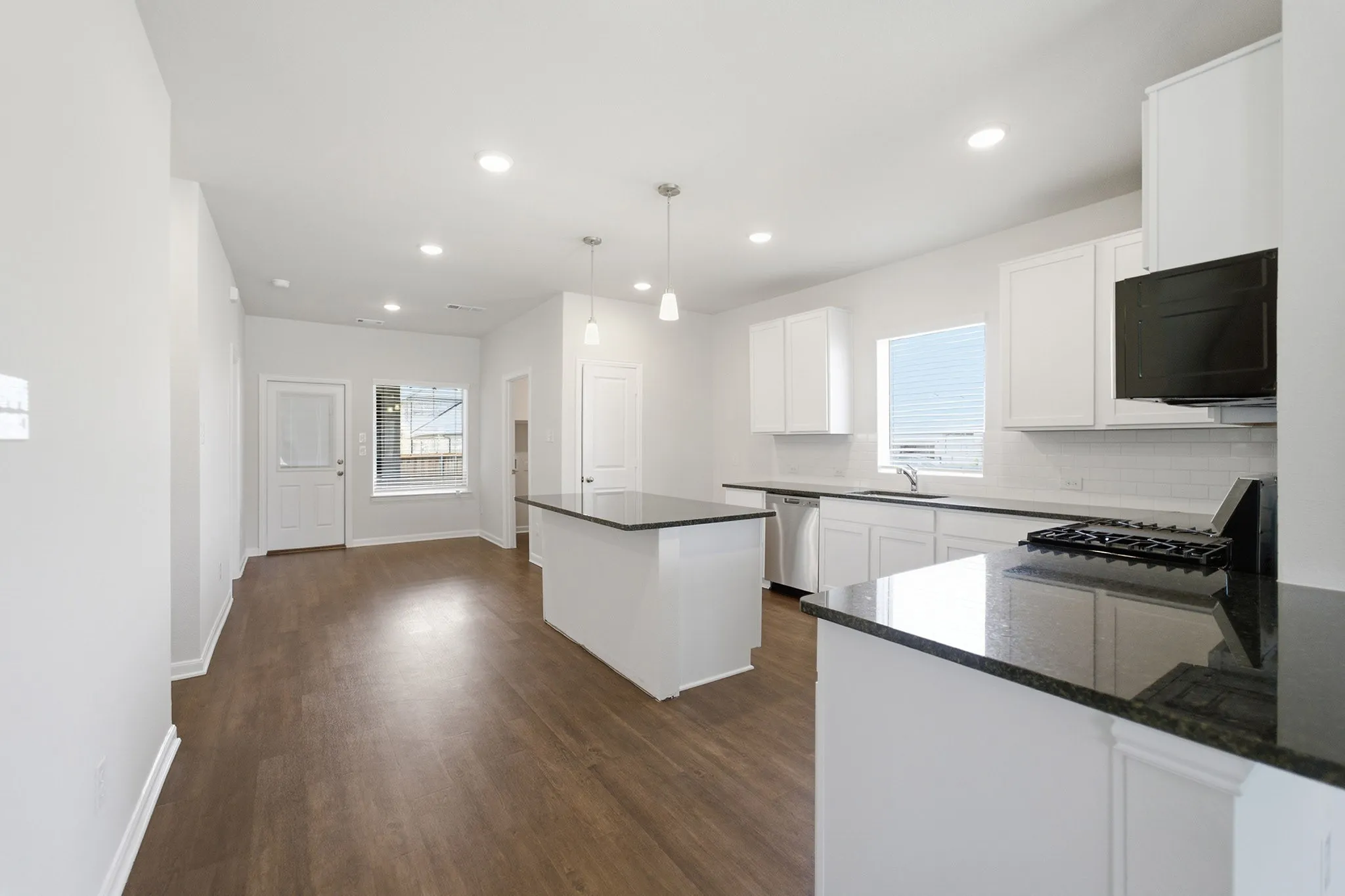 Open-concept kitchen featuring an island, white cabinetry, dark countertops, and wood-finish flooring