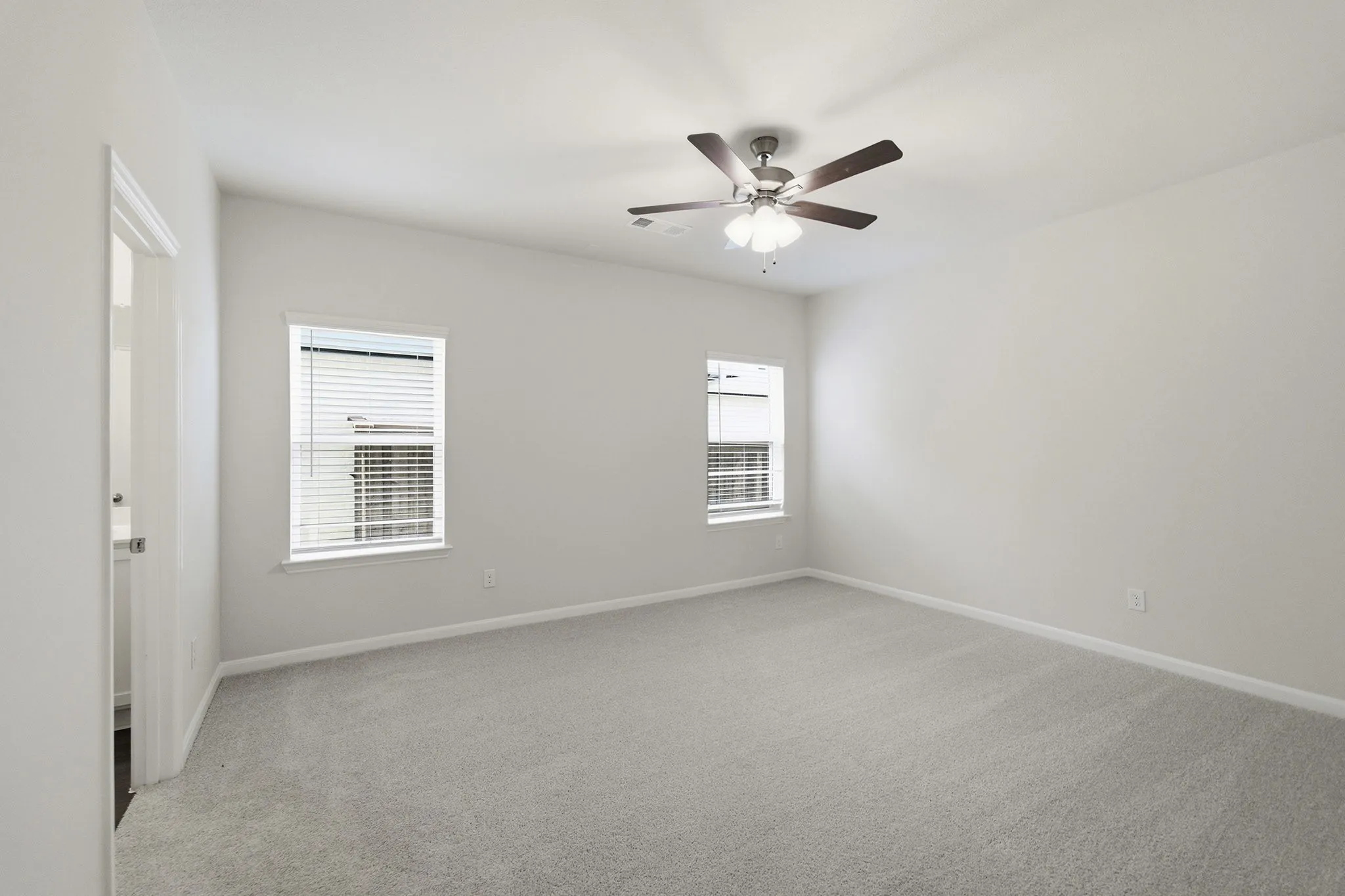 Spacious room featuring neutral carpeting, two windows with blinds, a ceiling fan with integrated lighting, and light-toned walls