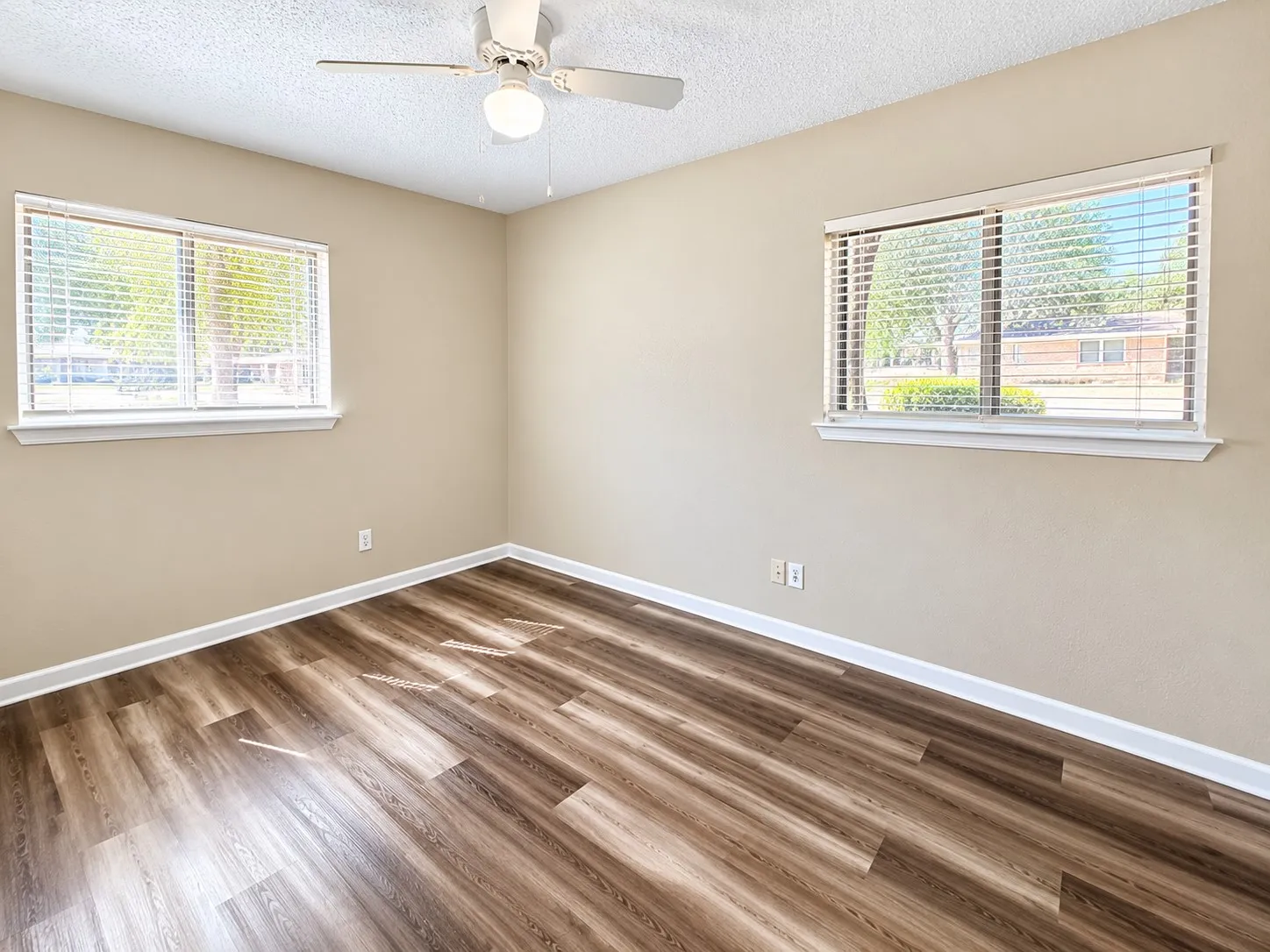 Wood-finish flooring, two large windows with blinds, ceiling fan with integrated lighting, and neutral wall paint