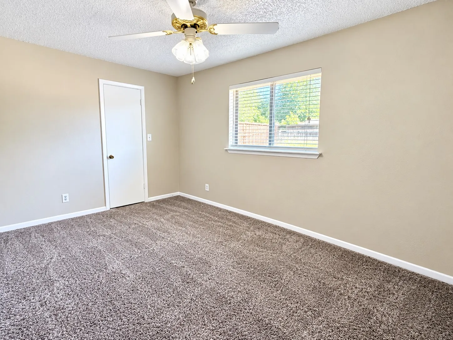 Neutral tone wall color, textured ceiling, brown patterned carpet, white window trim, and a ceiling fan with integrated lighting