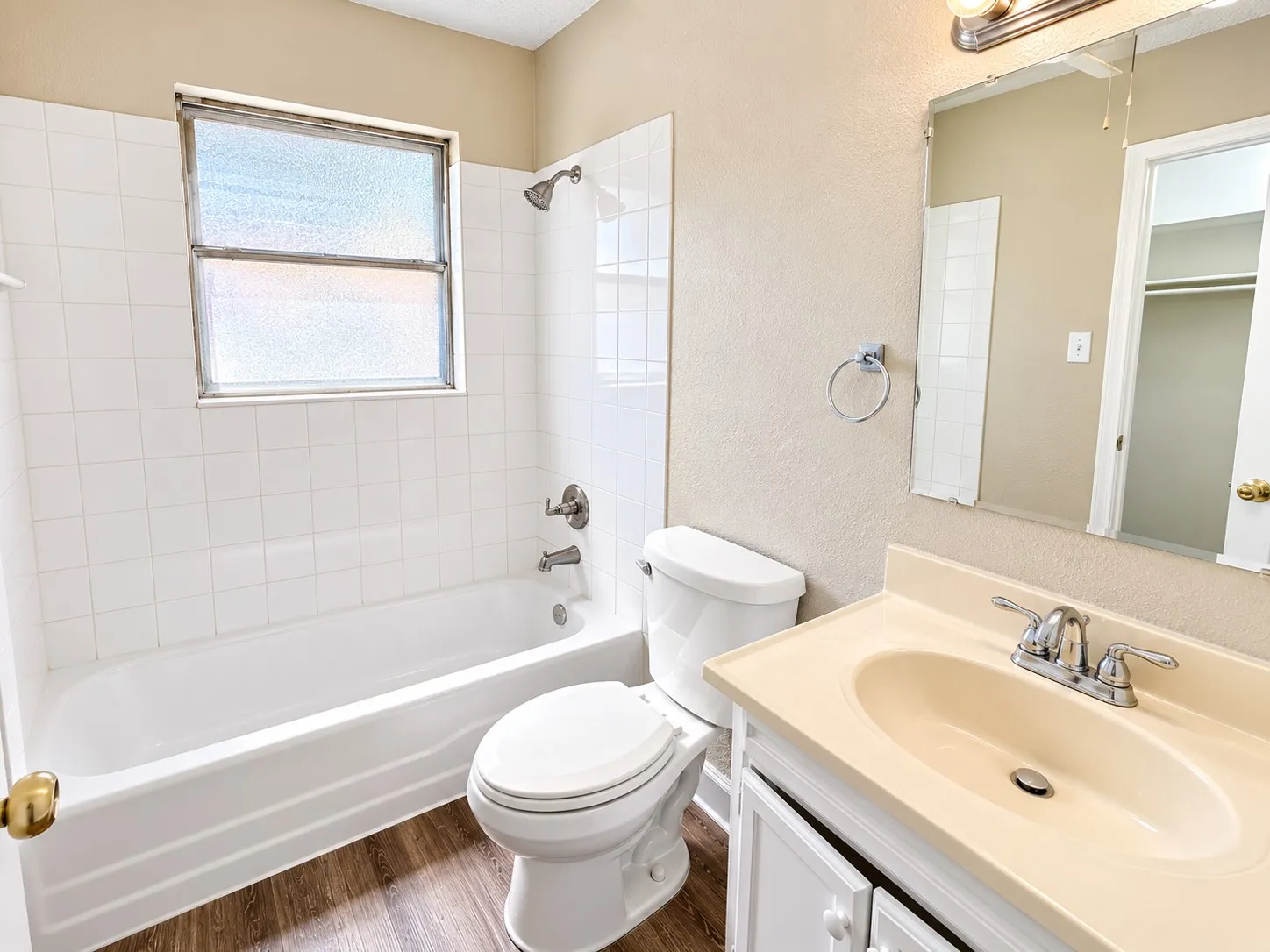 Bathroom featuring a single vanity, wood-finish flooring, a toilet, a tub, and tiled shower walls