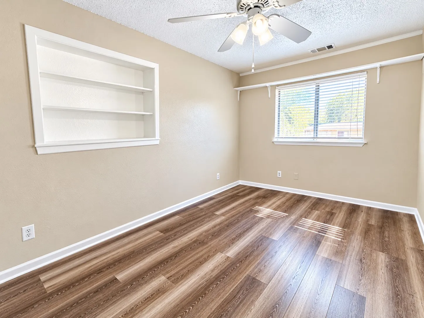 Wood-finish flooring, built-in shelving, ceiling fan, window with blinds, and white trim throughout