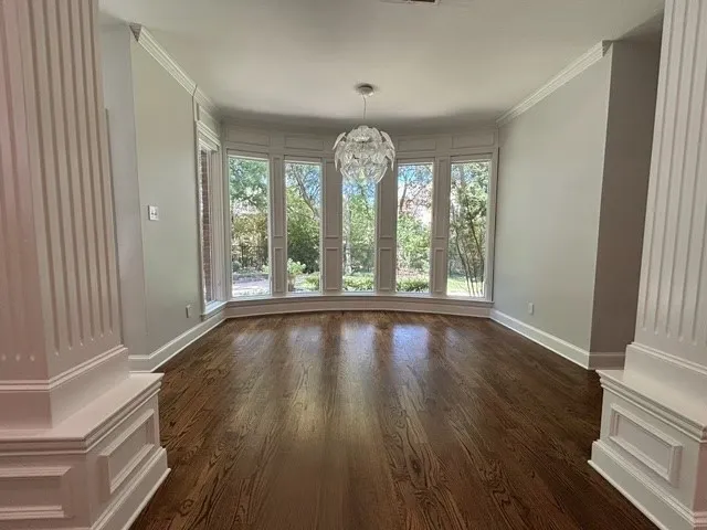 Hardwood flooring, bay window with multiple panes, decorative column, crown molding, and a contemporary light fixture