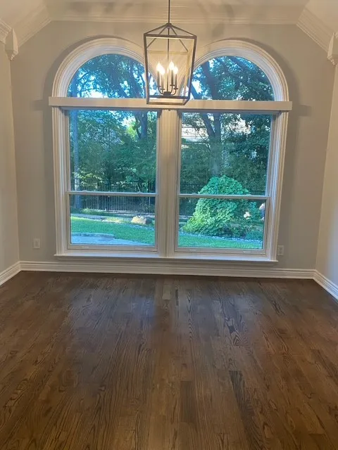 Hardwood flooring, arched windows, crown molding, and a black metal chandelier