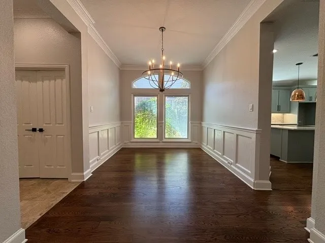 Wood-finish flooring, wainscoting wall accents, crown molding, arched transom window, and a bronze chandelier