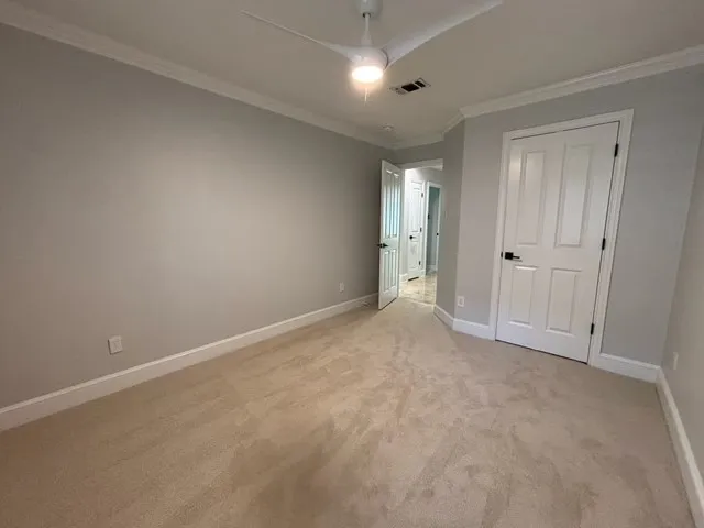 Neutral gray wall paint, crown molding, white trim, light-colored carpeting, and a modern ceiling fan with integrated lighting